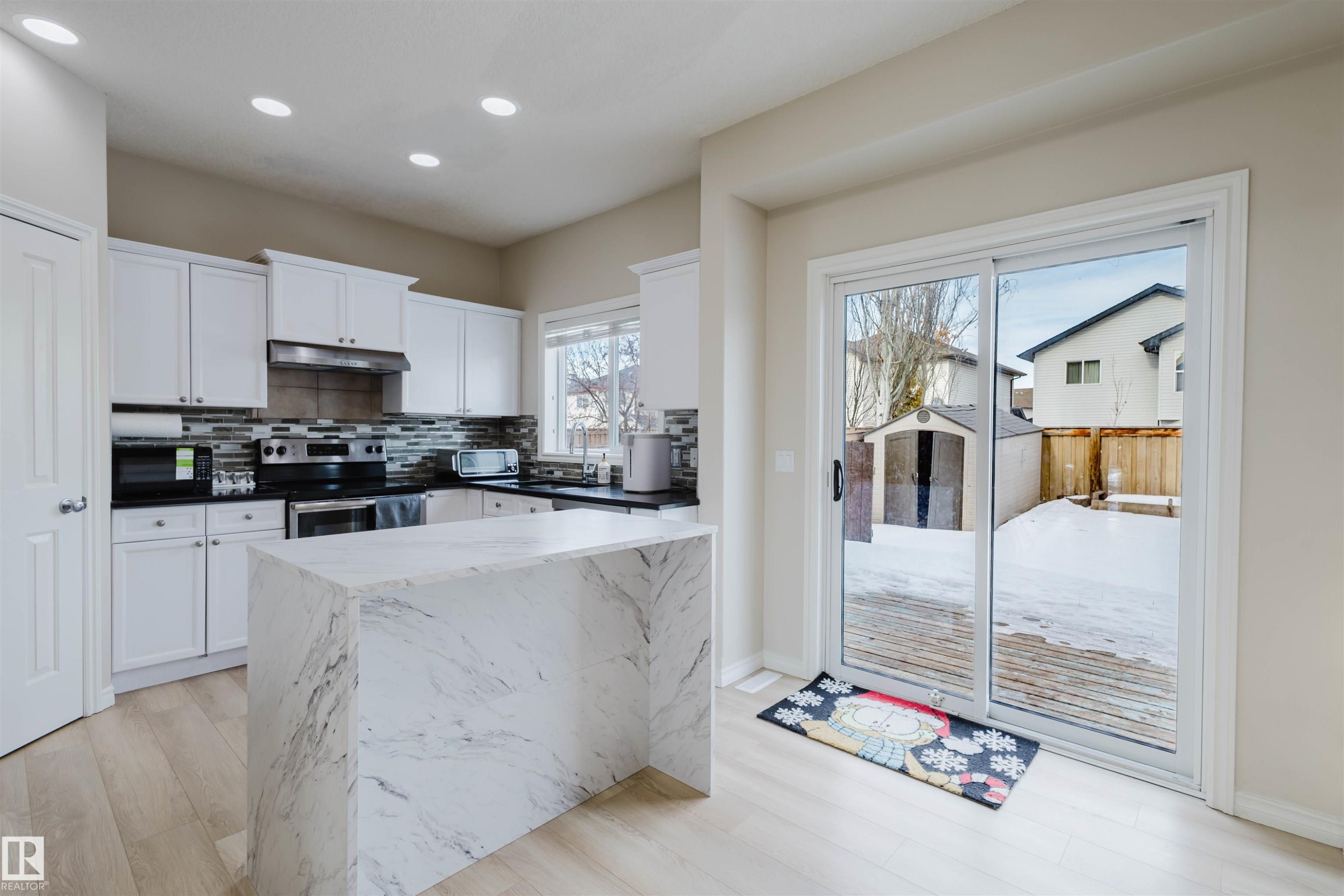 Kitchen with white cabinetry, electric stove, black microwave, light wood-type flooring, and tasteful backsplash - 8420 Sloane Crescent, Edmonton, AB - Indoor Photo Showing Kitchen
