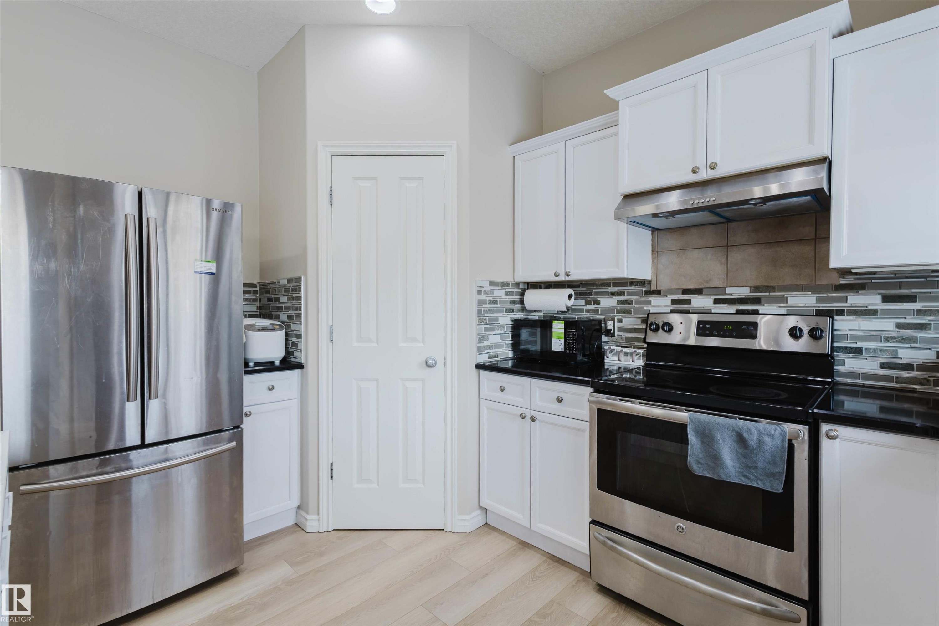 Kitchen featuring stainless steel appliances, white cabinetry, light wood-style floors, backsplash, and dark stone countertops - 8420 Sloane Crescent, Edmonton, AB - Indoor Photo Showing Kitchen With Upgraded Kitchen