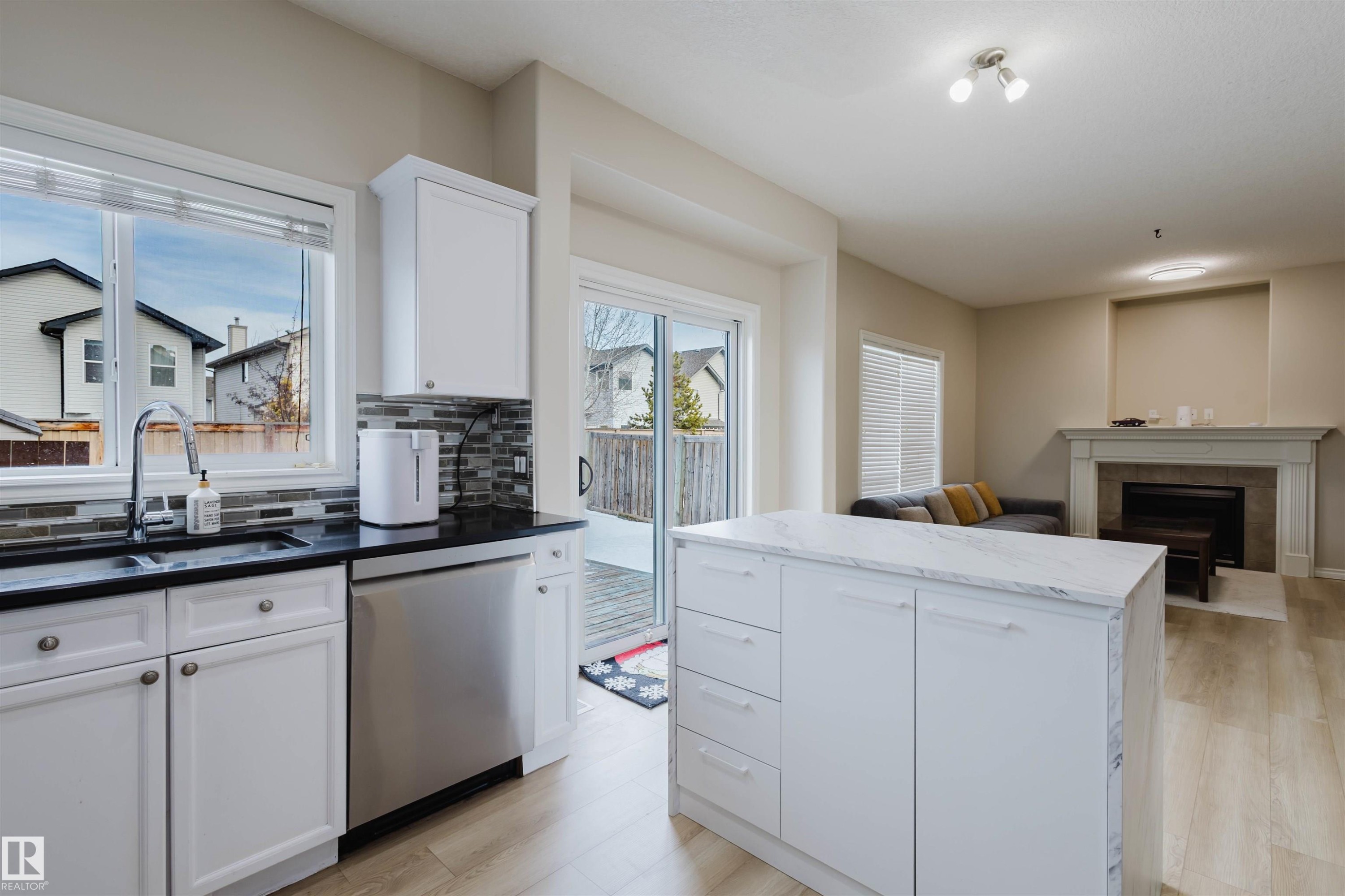 Kitchen featuring white cabinets, dishwasher, light wood-style flooring, backsplash, and open floor plan - 8420 Sloane Crescent, Edmonton, AB - Indoor Photo Showing Kitchen With Fireplace With Double Sink