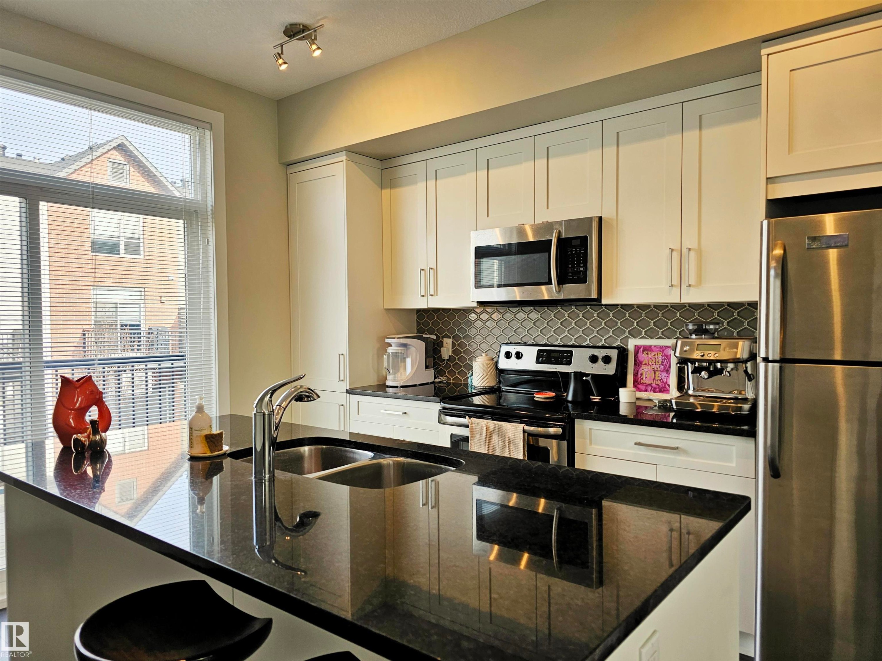 Kitchen with stainless steel appliances, white cabinetry, and dark stone counters - 129 2560 Pegasus Boulevard, Edmonton, AB - Indoor Photo Showing Kitchen With Double Sink With Upgraded Kitchen