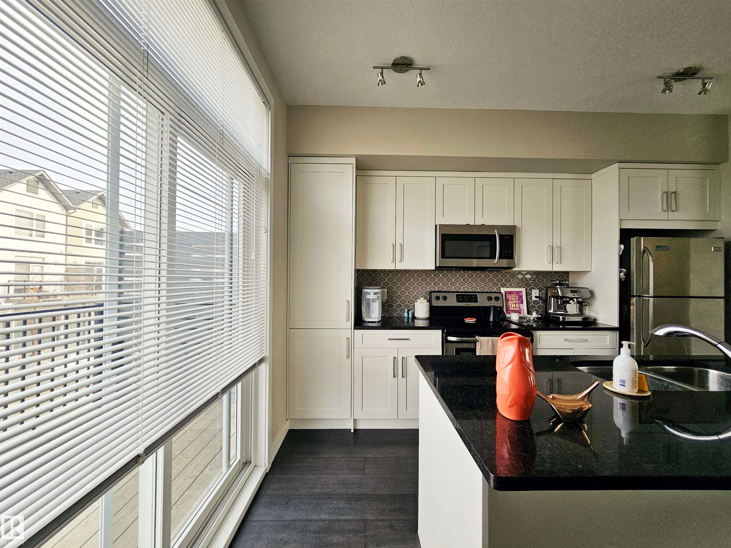 Kitchen featuring white cabinets, stainless steel appliances, dark stone counters, dark wood-style floors, and backsplash - 129 2560 Pegasus Boulevard, Edmonton, AB - Indoor Photo Showing Kitchen