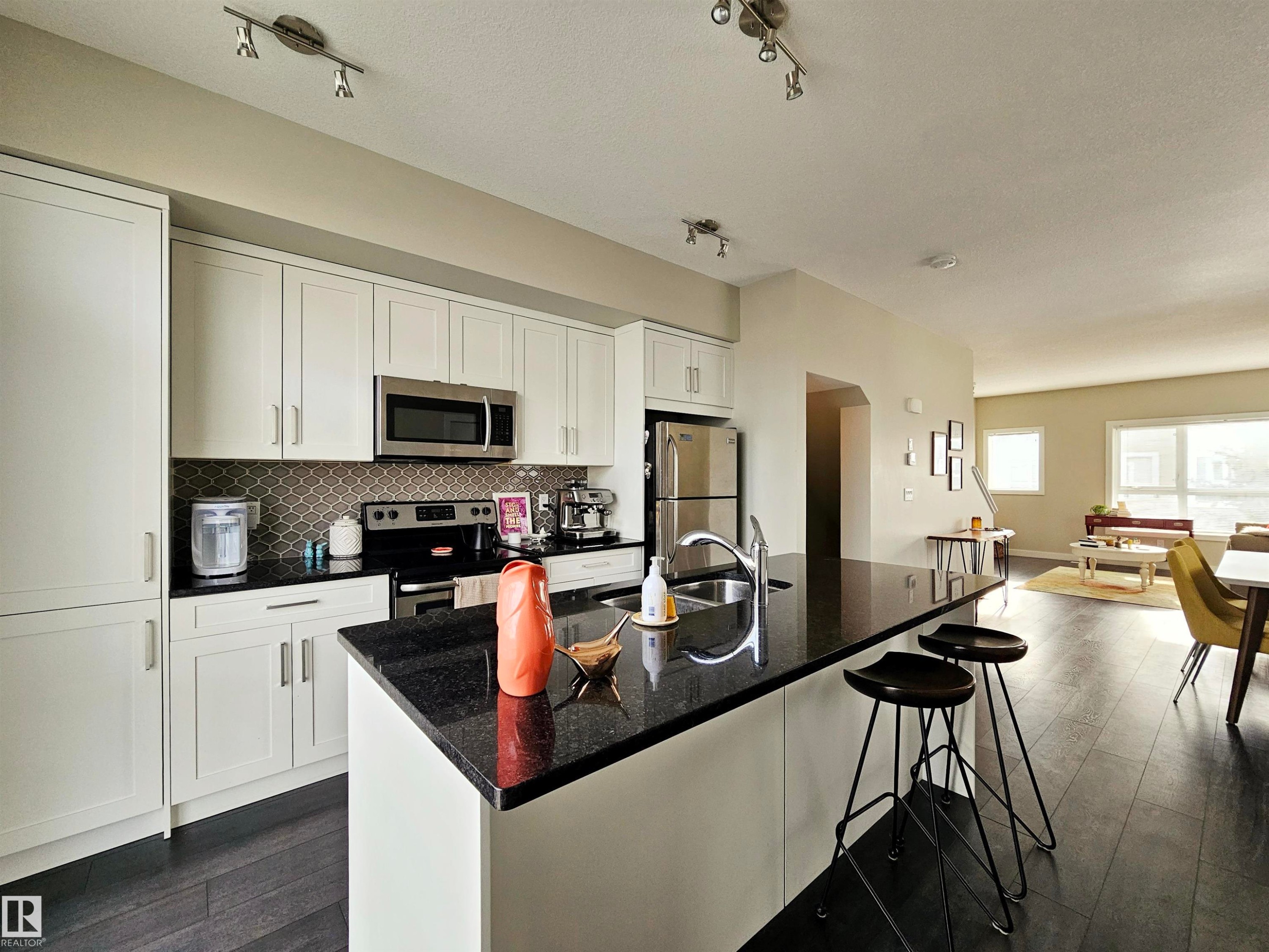 Kitchen featuring white cabinetry, dark wood finished floors, a breakfast bar, stainless steel appliances, and rail lighting - 129 2560 Pegasus Boulevard, Edmonton, AB - Indoor Photo Showing Kitchen With Upgraded Kitchen