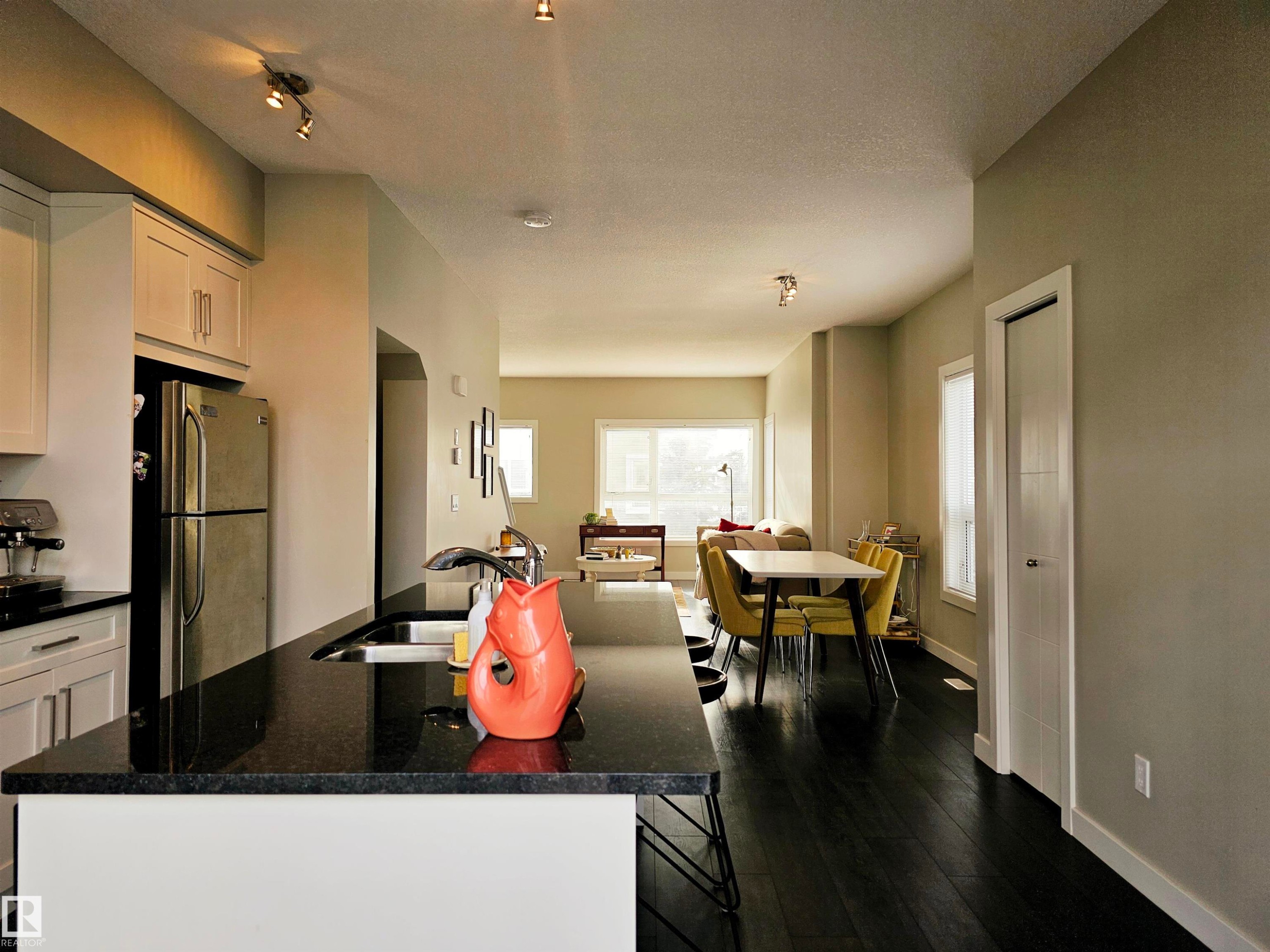 Kitchen featuring a center island with sink, freestanding refrigerator, dark wood-style flooring, white cabinets, and open floor plan - 129 2560 Pegasus Boulevard, Edmonton, AB - Indoor
