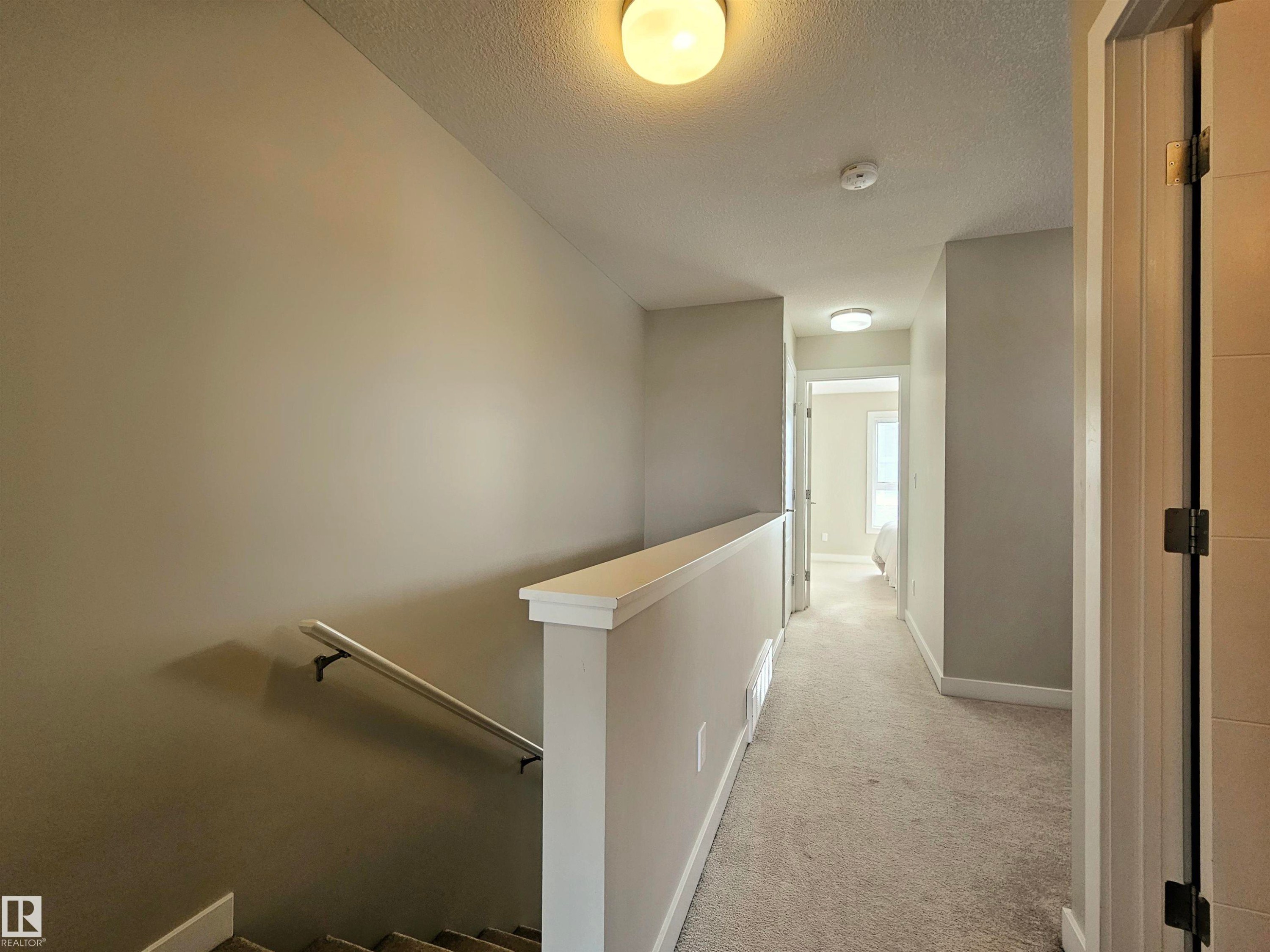 Hall featuring an upstairs landing, light carpet, and a textured ceiling - 129 2560 Pegasus Boulevard, Edmonton, AB - Indoor Photo Showing Other Room