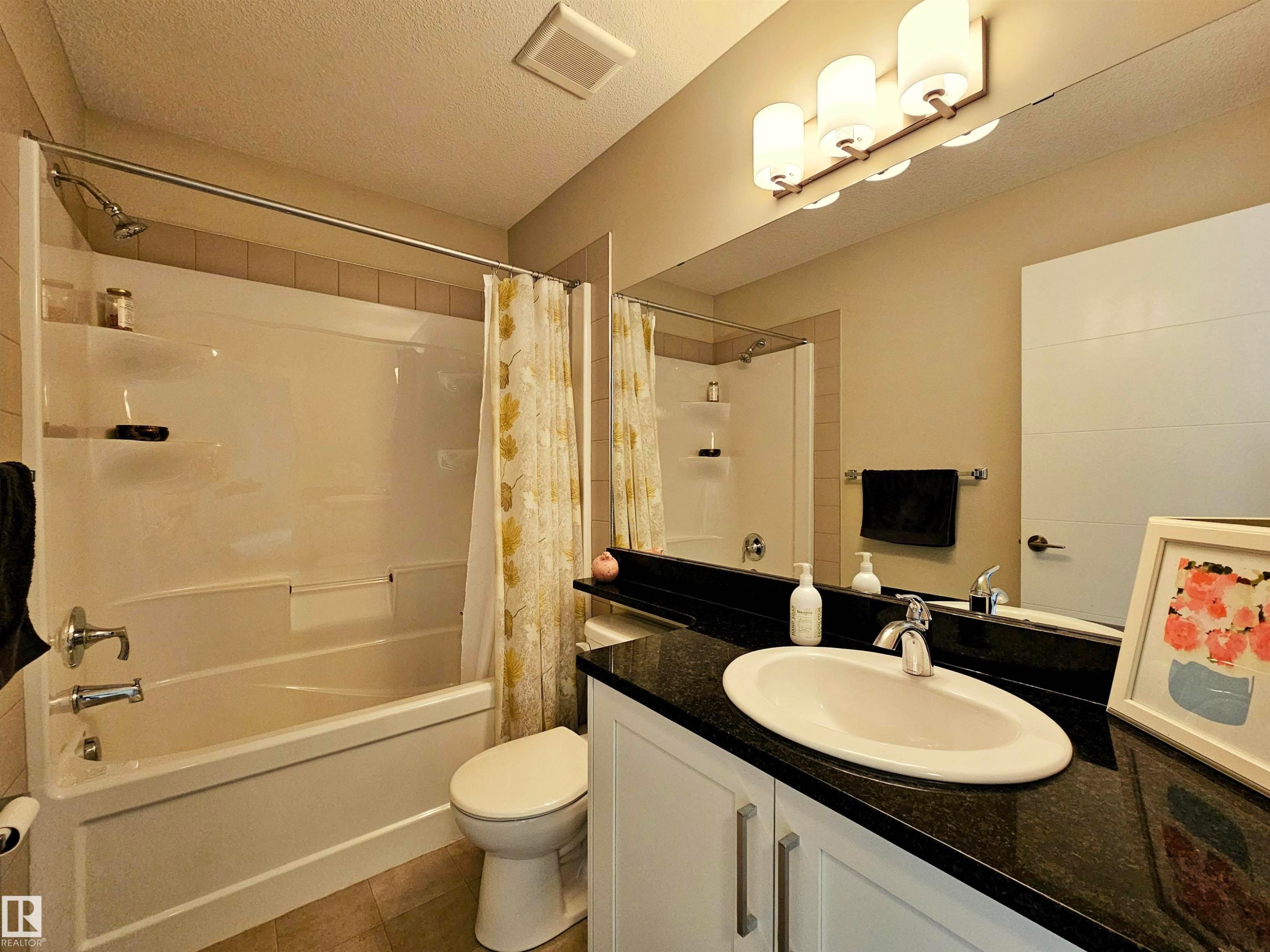 Bathroom with vanity, shower / bath combination with curtain, and a textured ceiling - 129 2560 Pegasus Boulevard, Edmonton, AB - Indoor Photo Showing Bathroom