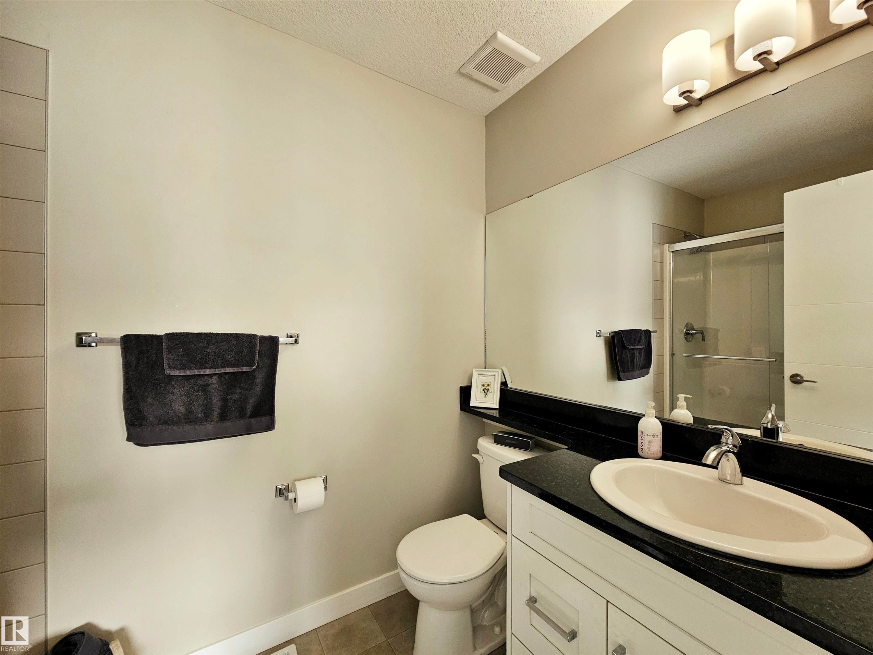 Bathroom with a stall shower, vanity, a textured ceiling, and dark tile patterned floors - 129 2560 Pegasus Boulevard, Edmonton, AB - Indoor Photo Showing Bathroom