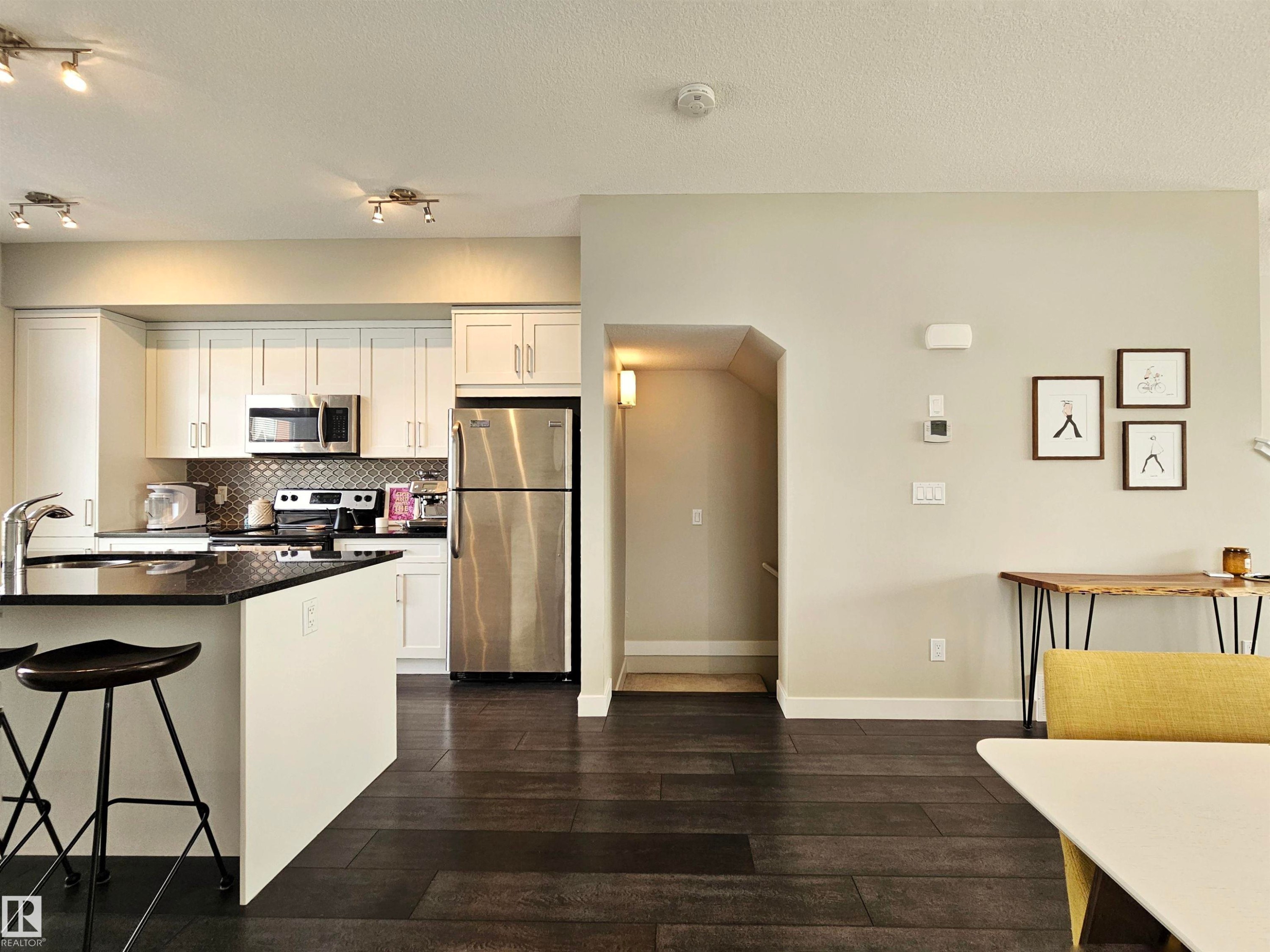 Kitchen with stainless steel appliances, dark wood-type flooring, white cabinetry, backsplash, and arched walkways - 129 2560 Pegasus Boulevard, Edmonton, AB - Indoor Photo Showing Kitchen