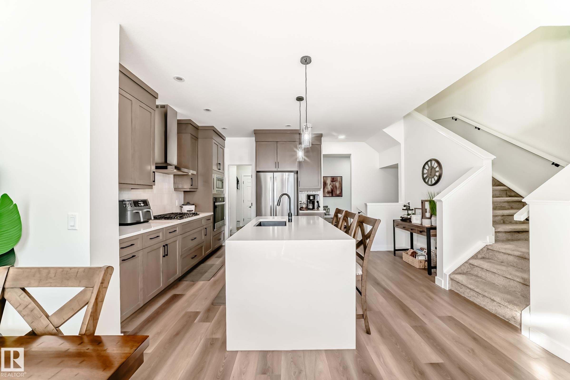 Kitchen featuring decorative light fixtures, a kitchen breakfast bar, an island with sink, light wood-type flooring, and stainless steel appliances - 3569 Erlanger Link, Edmonton, AB - Indoor