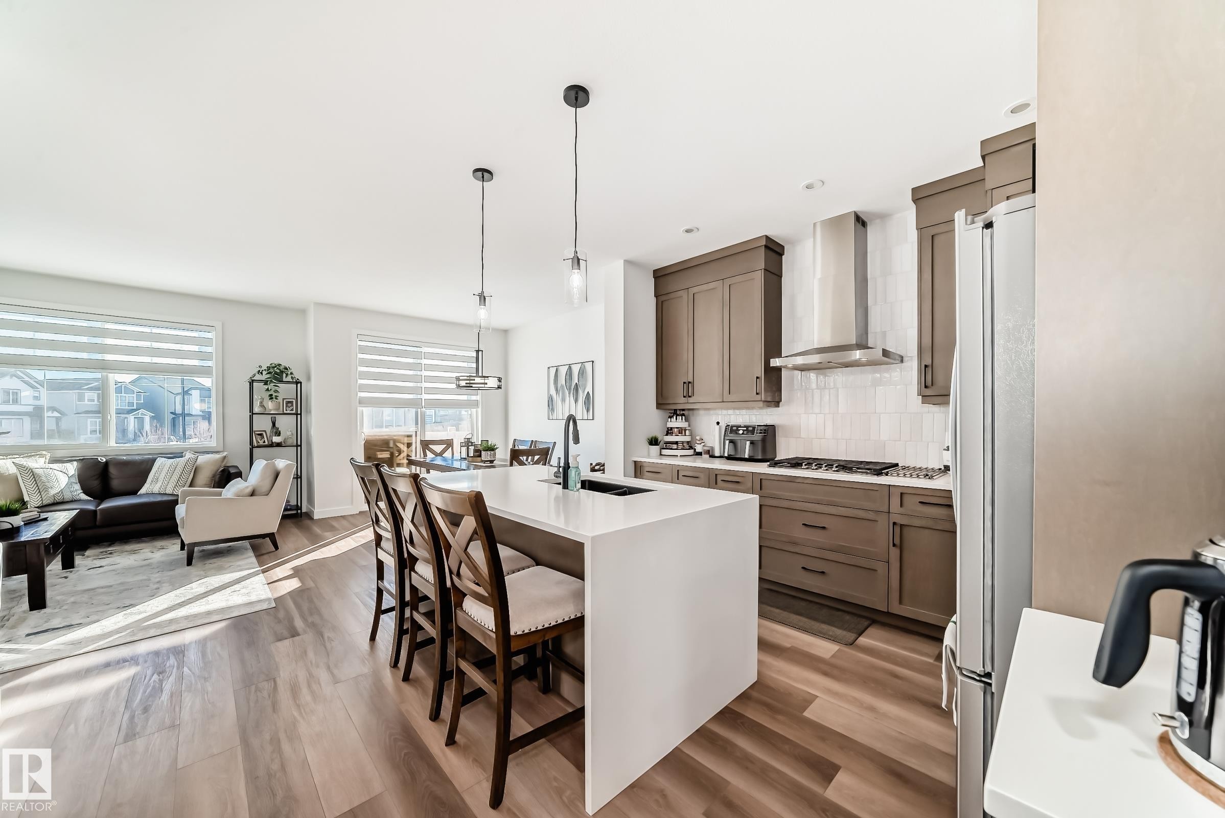 Kitchen featuring decorative light fixtures, decorative backsplash, a breakfast bar, light wood-type flooring, and light stone counters - 3569 Erlanger Link, Edmonton, AB - Indoor