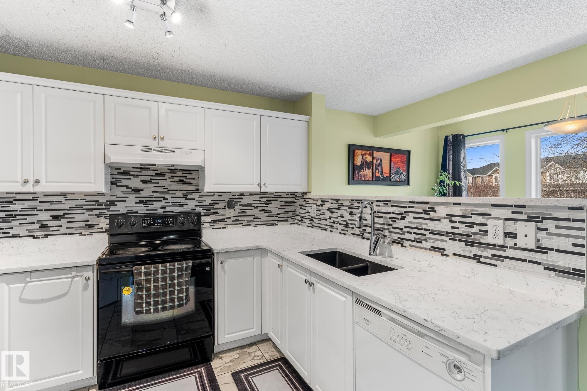 Kitchen with black electric range oven, white cabinetry, dishwasher, and a textured ceiling - 13148 151 Avenue, Edmonton, AB - Indoor Photo Showing Kitchen With Double Sink