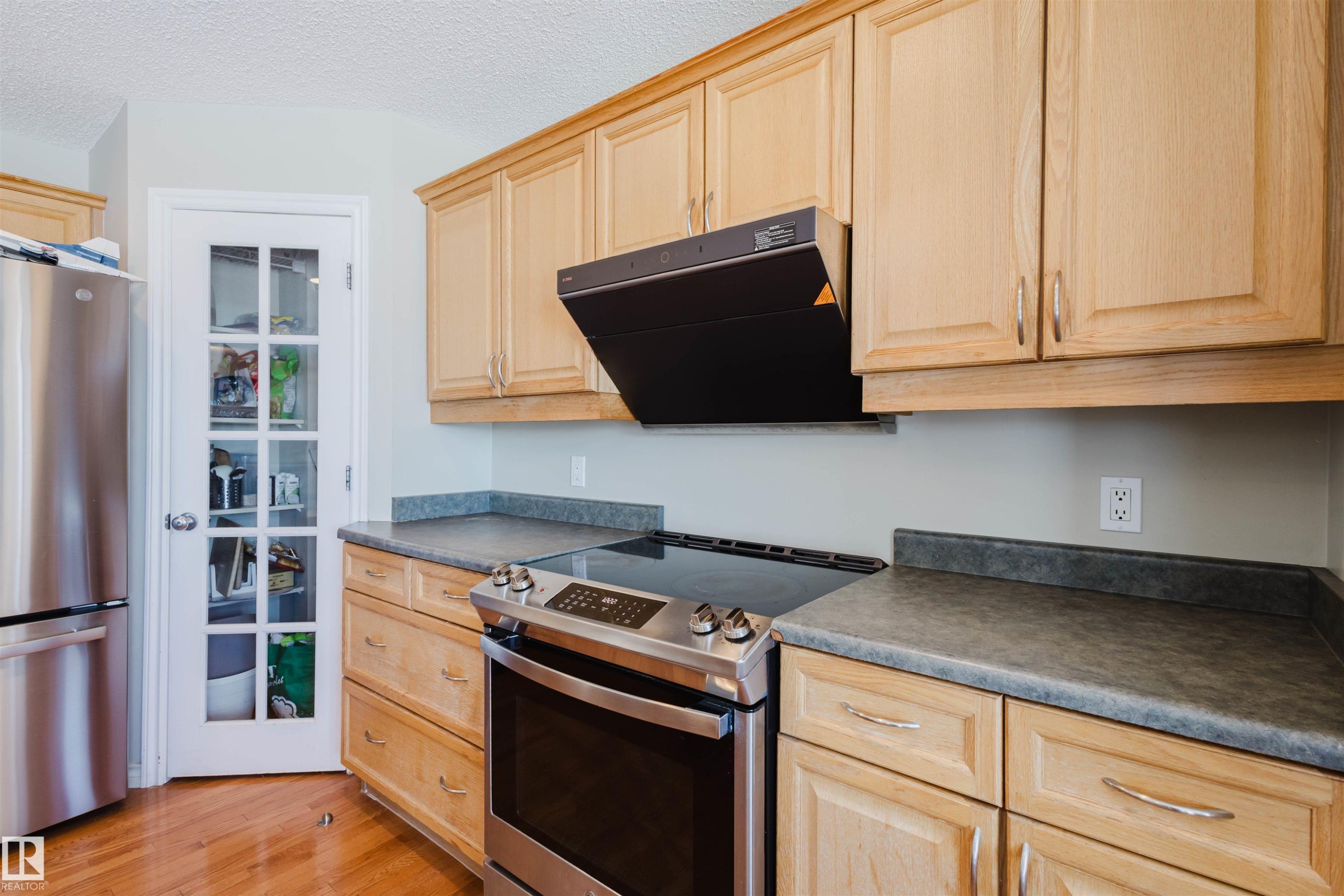 Kitchen with dark countertops, stainless steel appliances, light wood finish cabinets, ventilation hood, and a textured ceiling - 3534 Mclean Crescent, Edmonton, AB - Indoor Photo Showing Kitchen