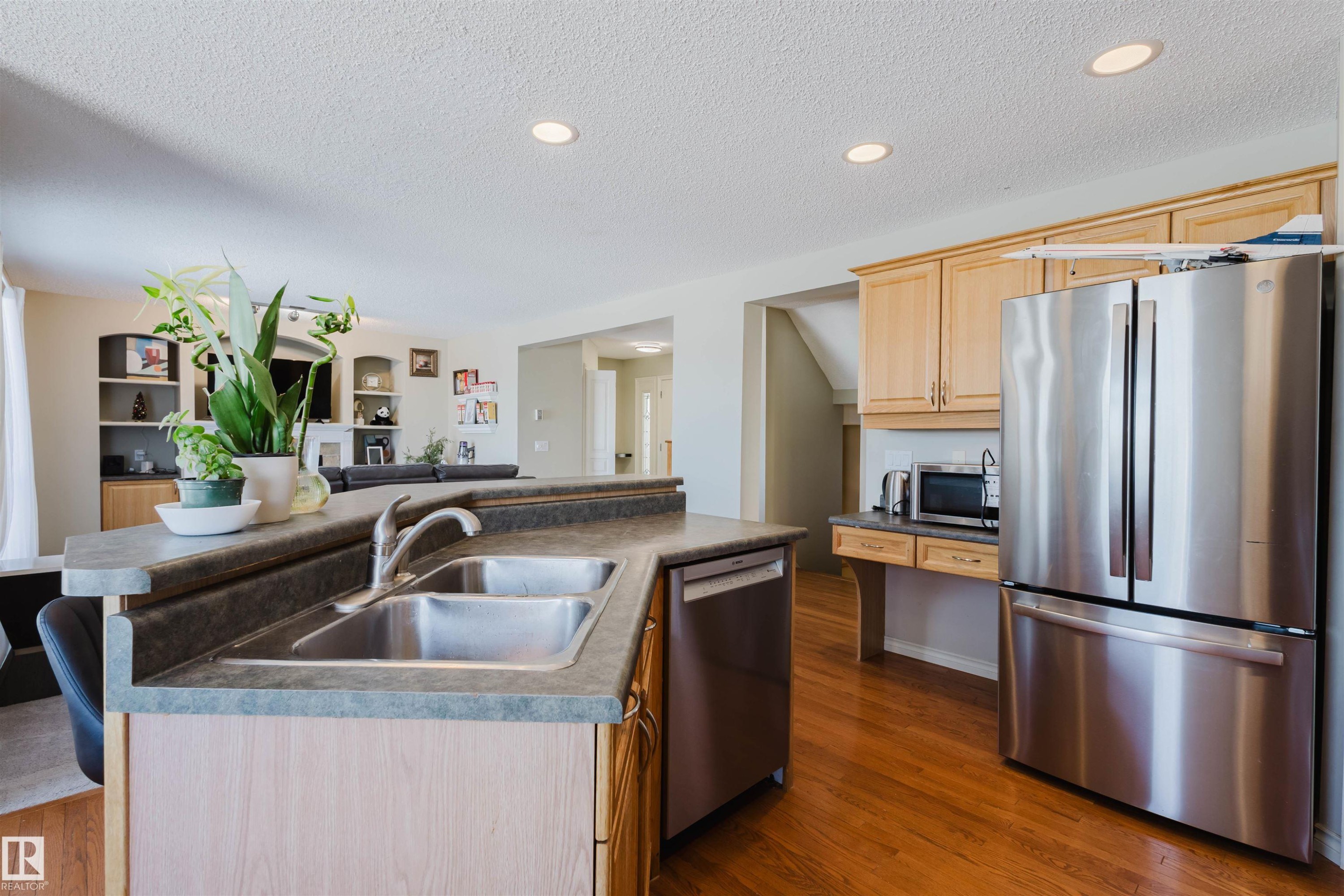 Kitchen with stainless steel appliances, dark countertops, light wood finish cabinets, dark wood-style floors, and an island with sink - 3534 Mclean Crescent, Edmonton, AB - Indoor Photo Showing Kitchen With Double Sink