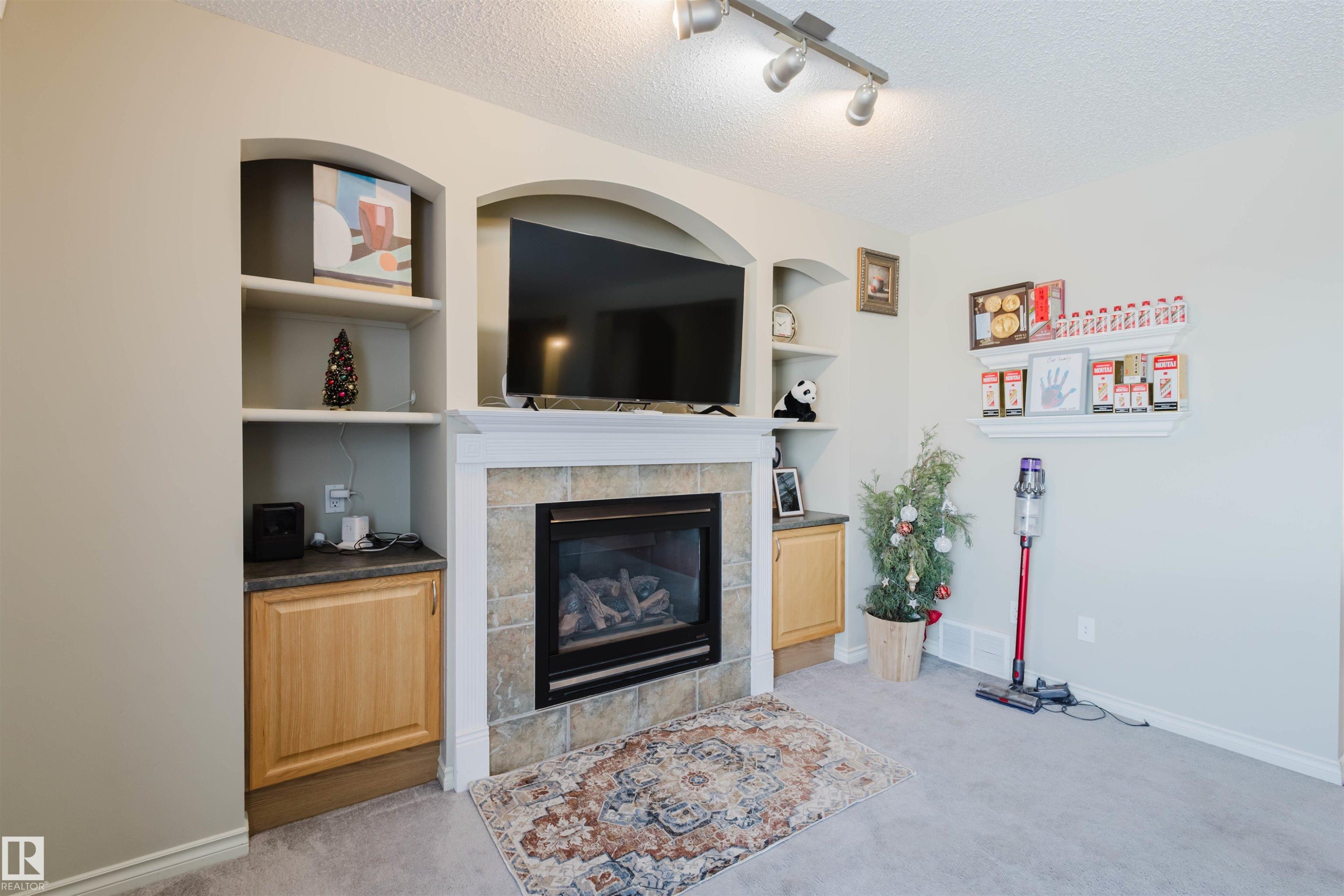 Living area featuring light colored carpet, built in shelves, a tiled fireplace, a textured ceiling, and rail lighting - 3534 Mclean Crescent, Edmonton, AB - Indoor Photo Showing Living Room With Fireplace