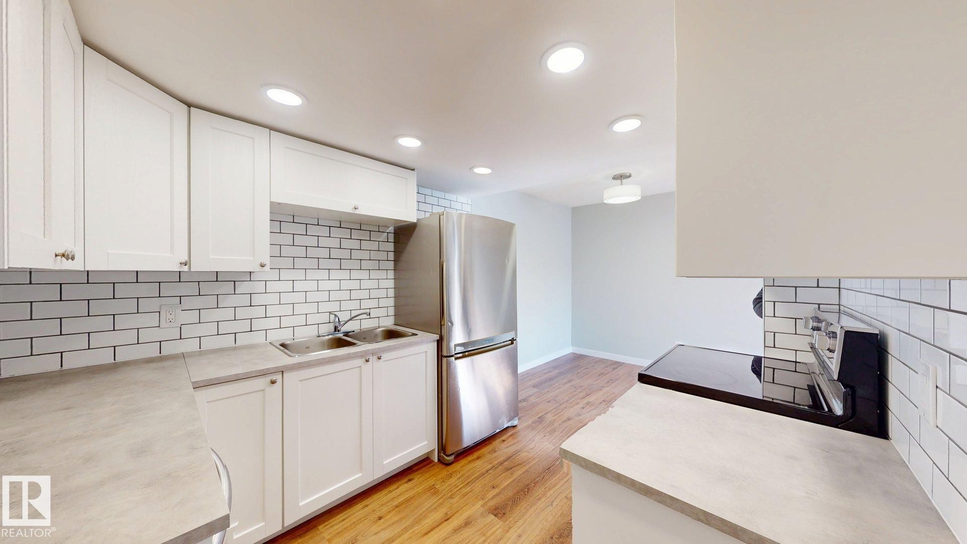 Kitchen with decorative backsplash, light countertops, white cabinets, light wood-style floors, and recessed lighting - 611 2908 116A Avenue, Edmonton, AB - Indoor Photo Showing Kitchen With Double Sink With Upgraded Kitchen