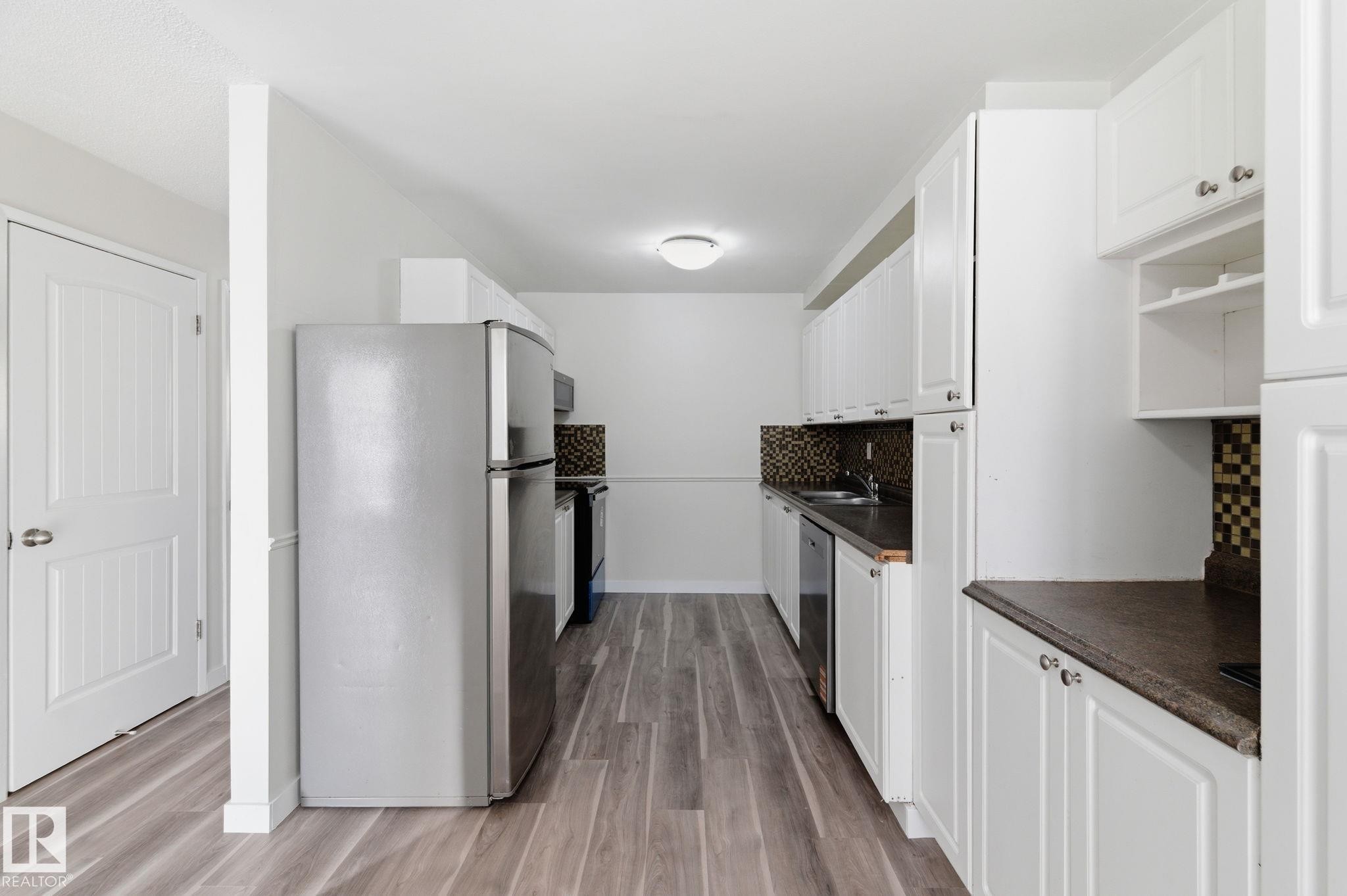 Kitchen featuring stainless steel appliances, tasteful backsplash, white cabinets, dark countertops, and light wood finished floors - 180 Londonderry Square, Edmonton, AB - Indoor Photo Showing Kitchen