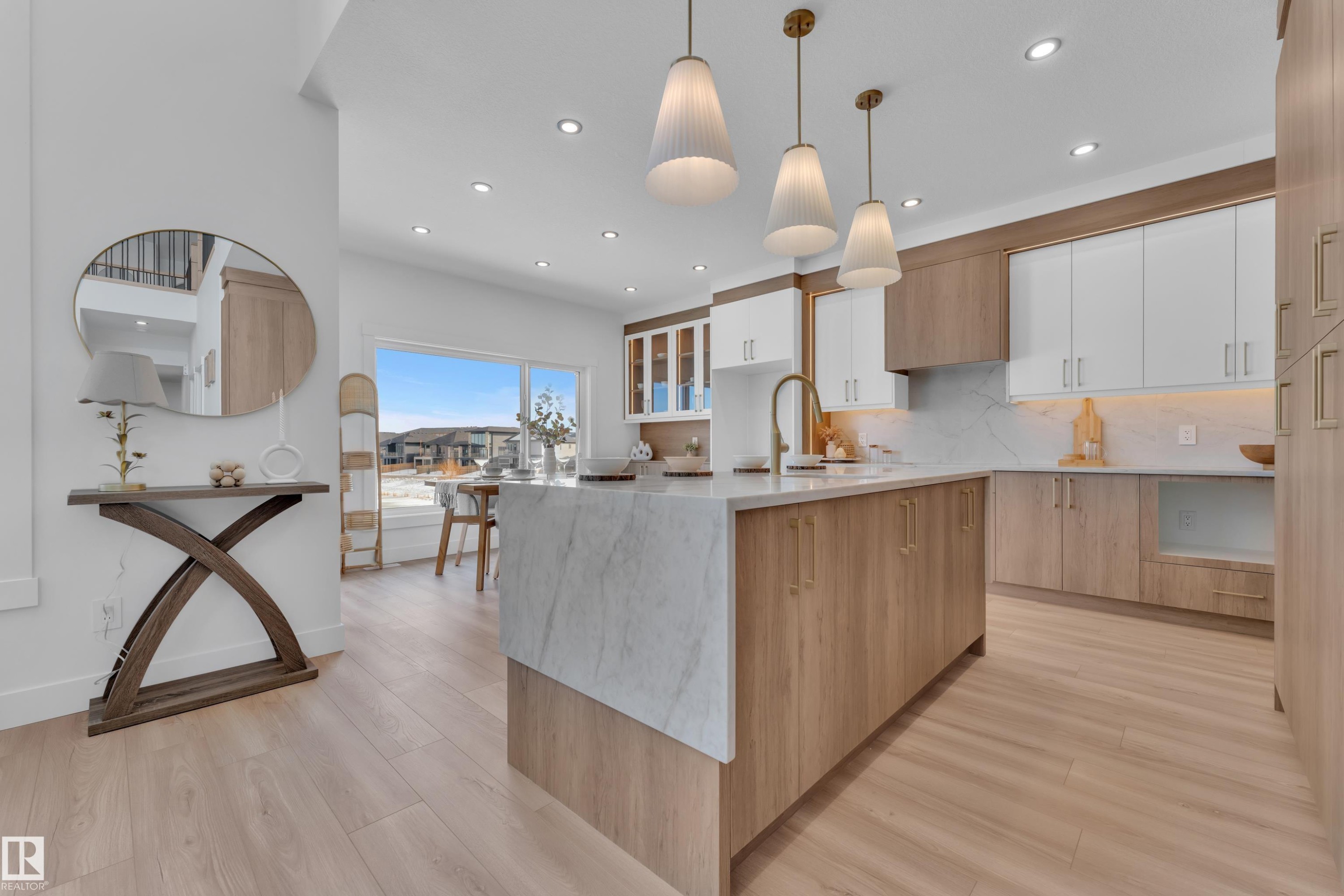 Dual tone kitchen with two tone cabinetry, a kitchen island with sink, light stone countertops, light wood-style floors, and hanging light fixtures - 228 Linden Loop, Leduc, AB - Indoor Photo Showing Kitchen With Upgraded Kitchen