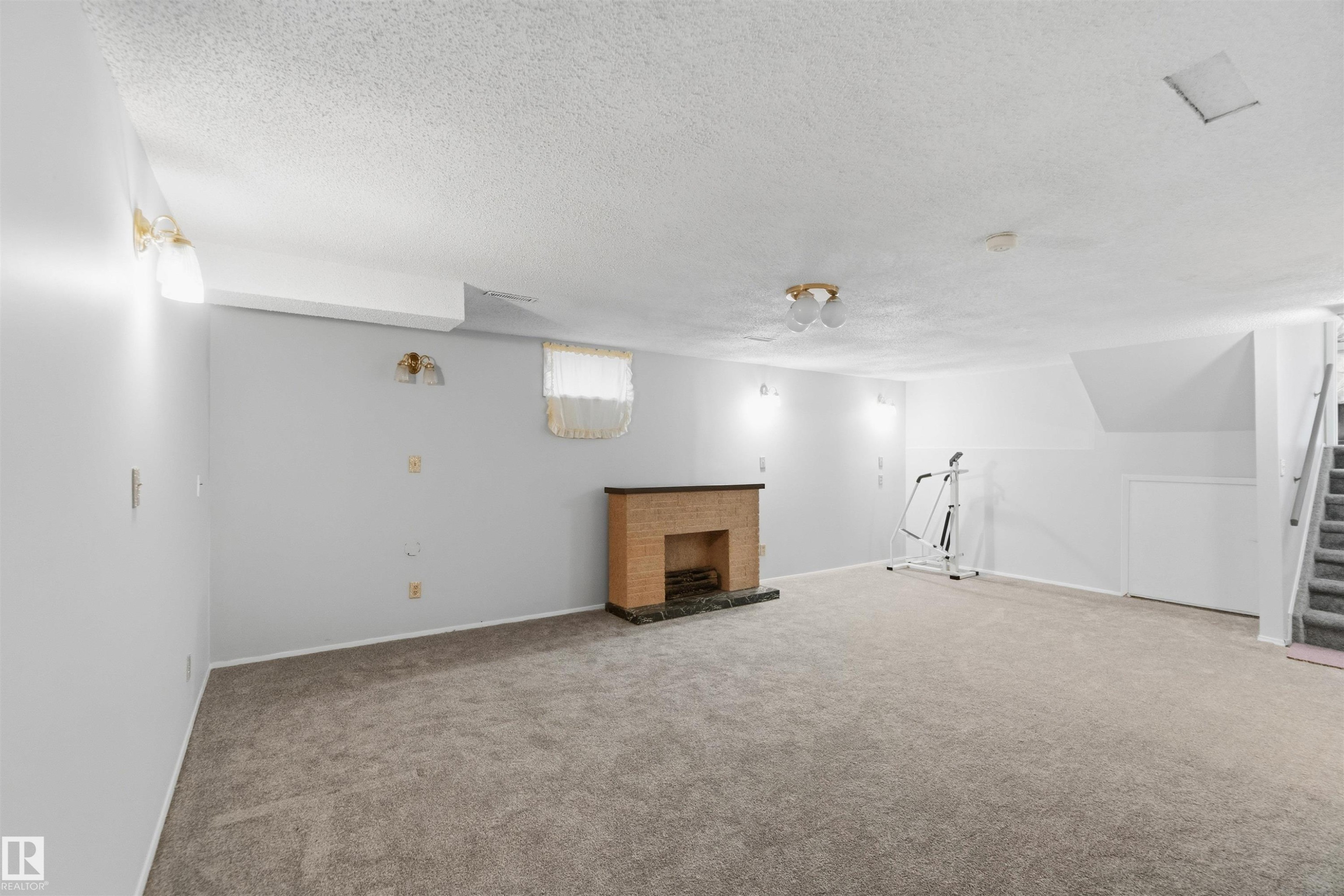 Basement with carpet flooring, a fireplace, and a textured ceiling - 135 Humberstone Road, Edmonton, AB - Indoor