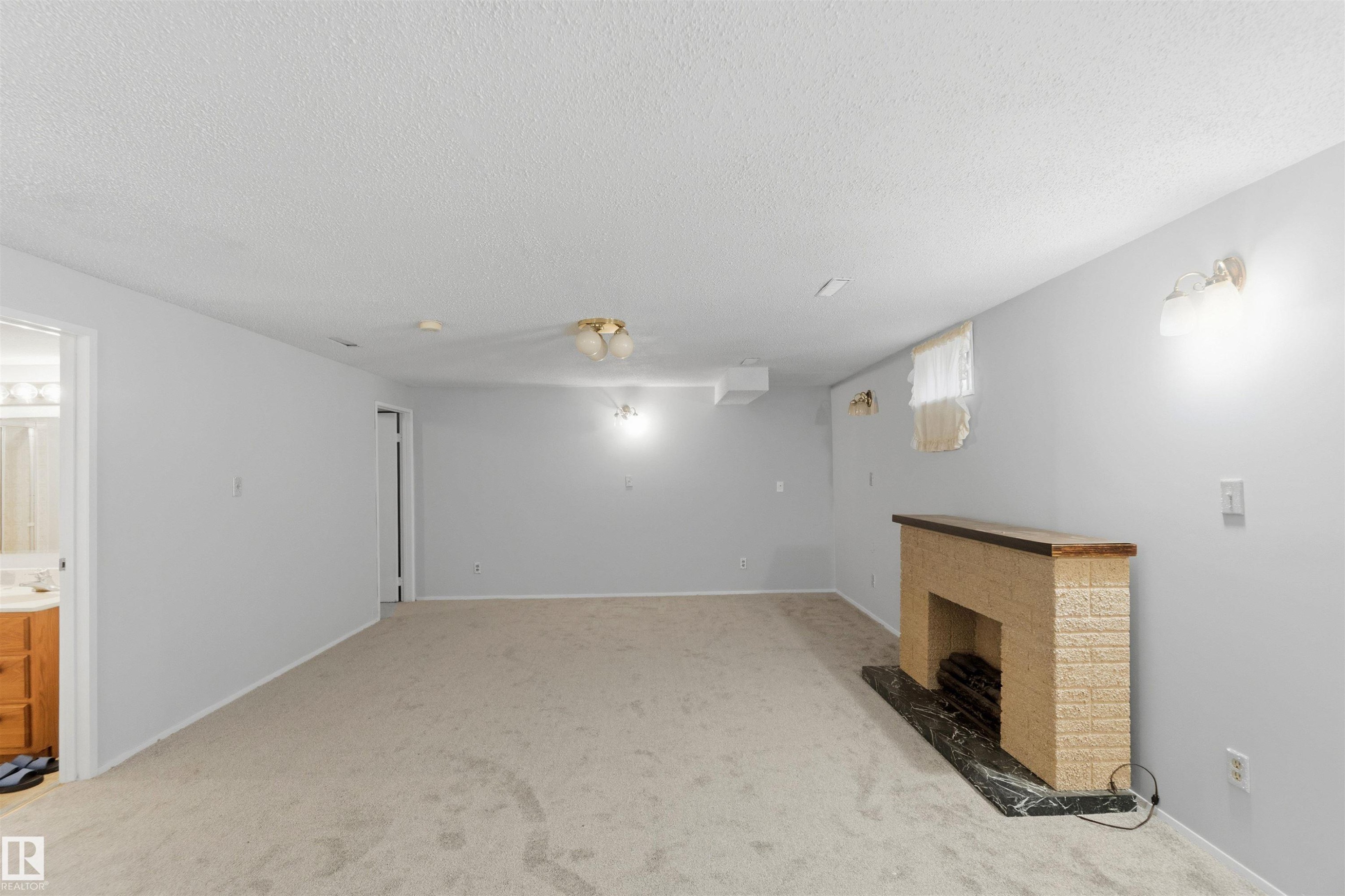Below grade area with light colored carpet, a brick fireplace, and a textured ceiling - 135 Humberstone Road, Edmonton, AB - Indoor