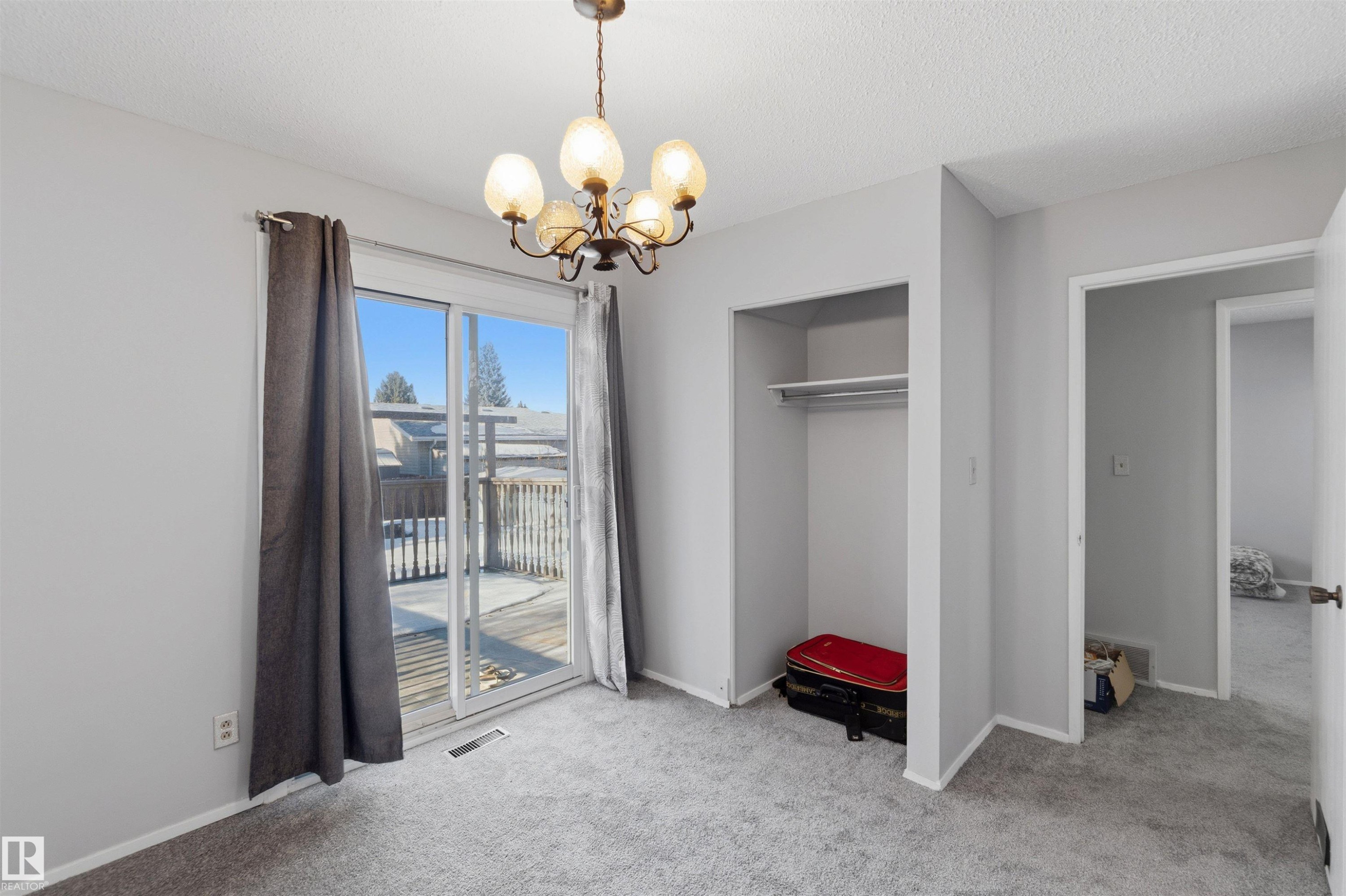 Unfurnished bedroom featuring a chandelier, light carpet, access to outside, a closet, and a textured ceiling - 135 Humberstone Road, Edmonton, AB - Indoor