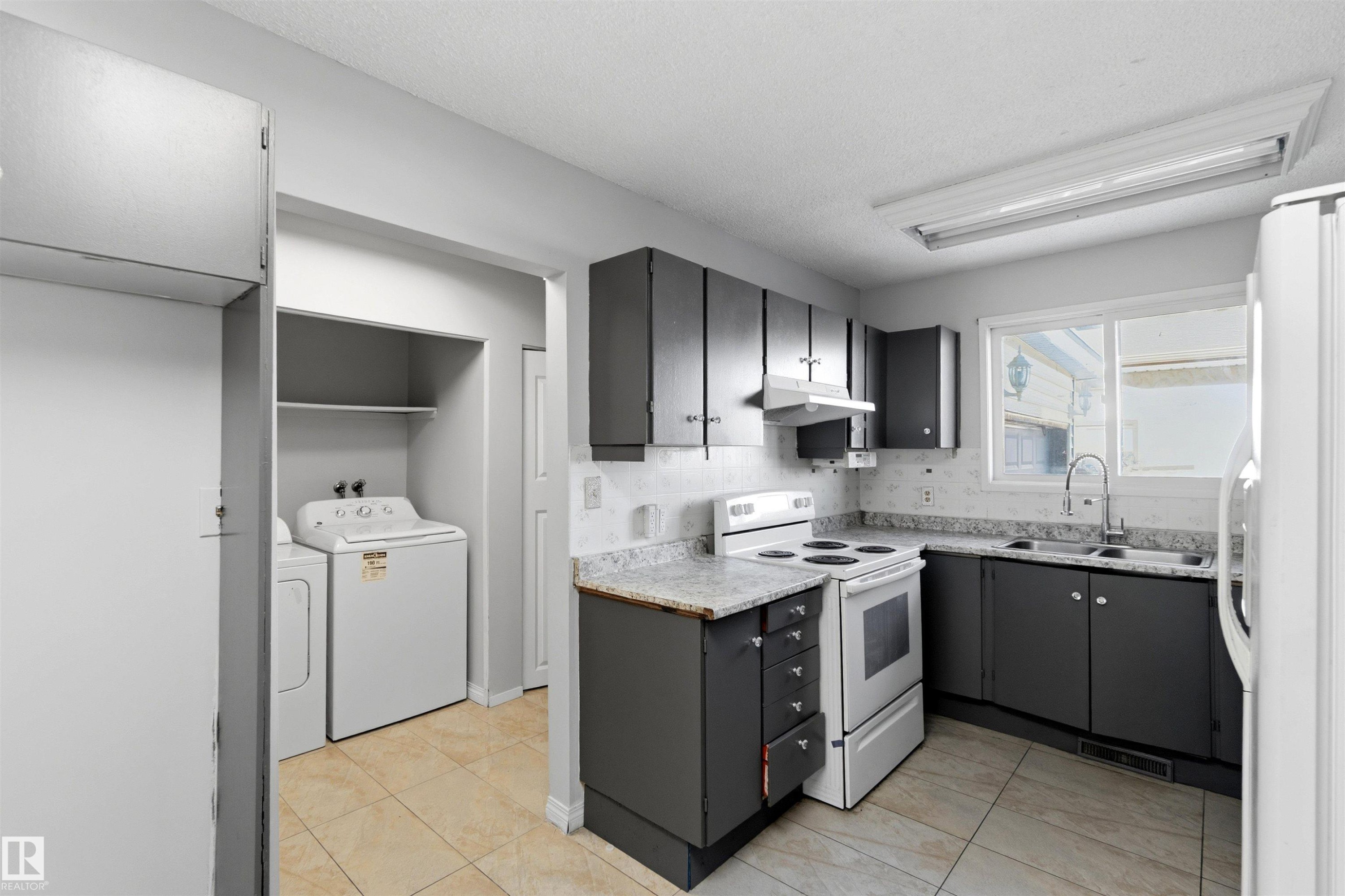 Kitchen with white appliances, light countertops, washer and dryer, decorative backsplash, and light tile patterned floors - 135 Humberstone Road, Edmonton, AB - Indoor