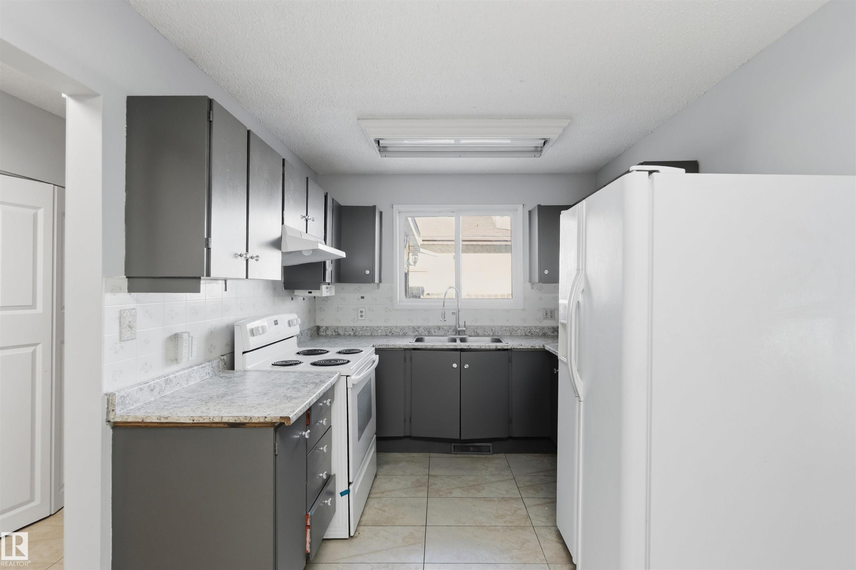 Kitchen featuring white appliances, gray cabinets, light countertops, light tile patterned floors, and backsplash - 135 Humberstone Road, Edmonton, AB - Indoor Photo Showing Kitchen With Double Sink
