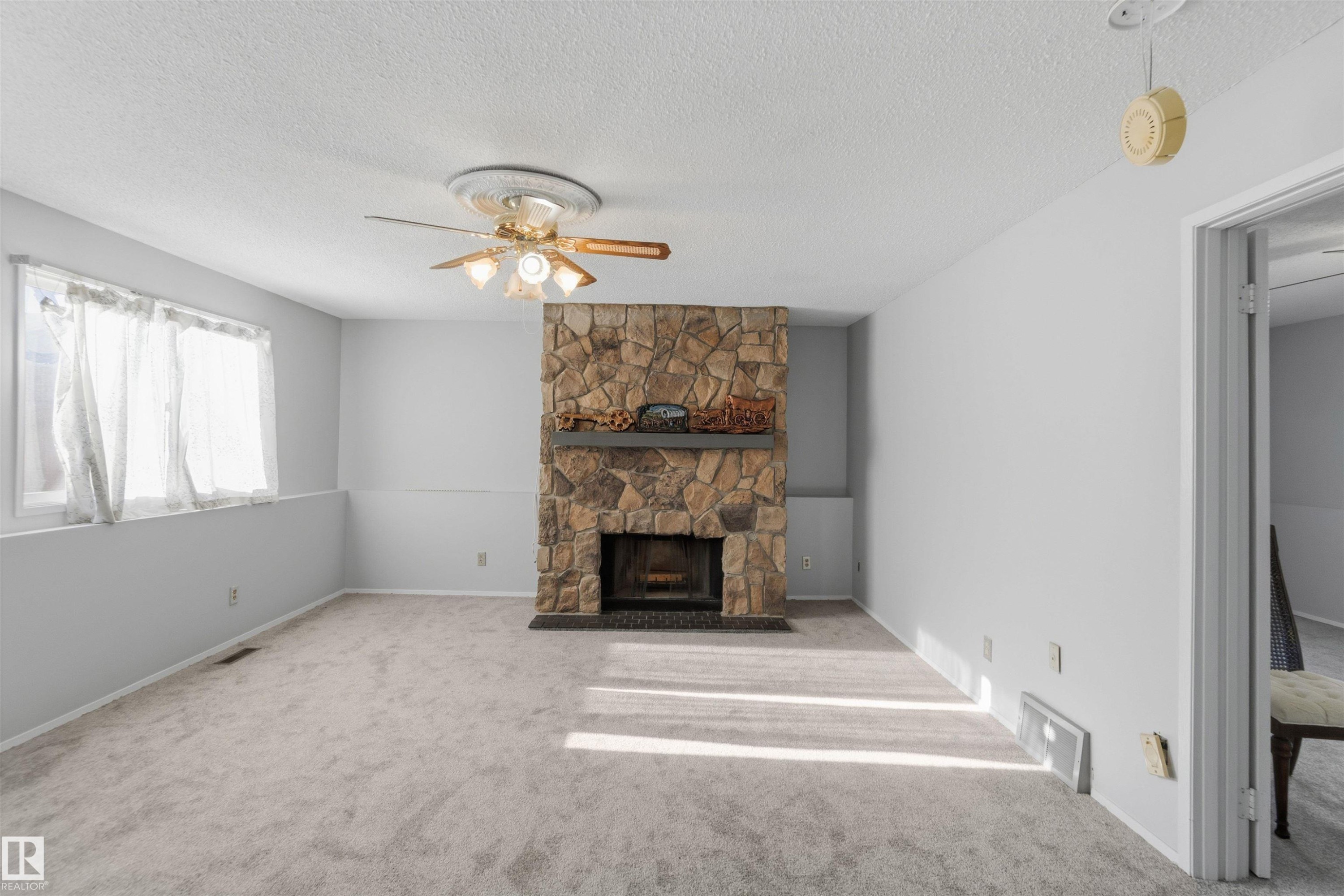 Unfurnished living room featuring a textured ceiling, a ceiling fan, carpet floors, and a fireplace - 135 Humberstone Road, Edmonton, AB - Indoor Photo Showing Living Room With Fireplace