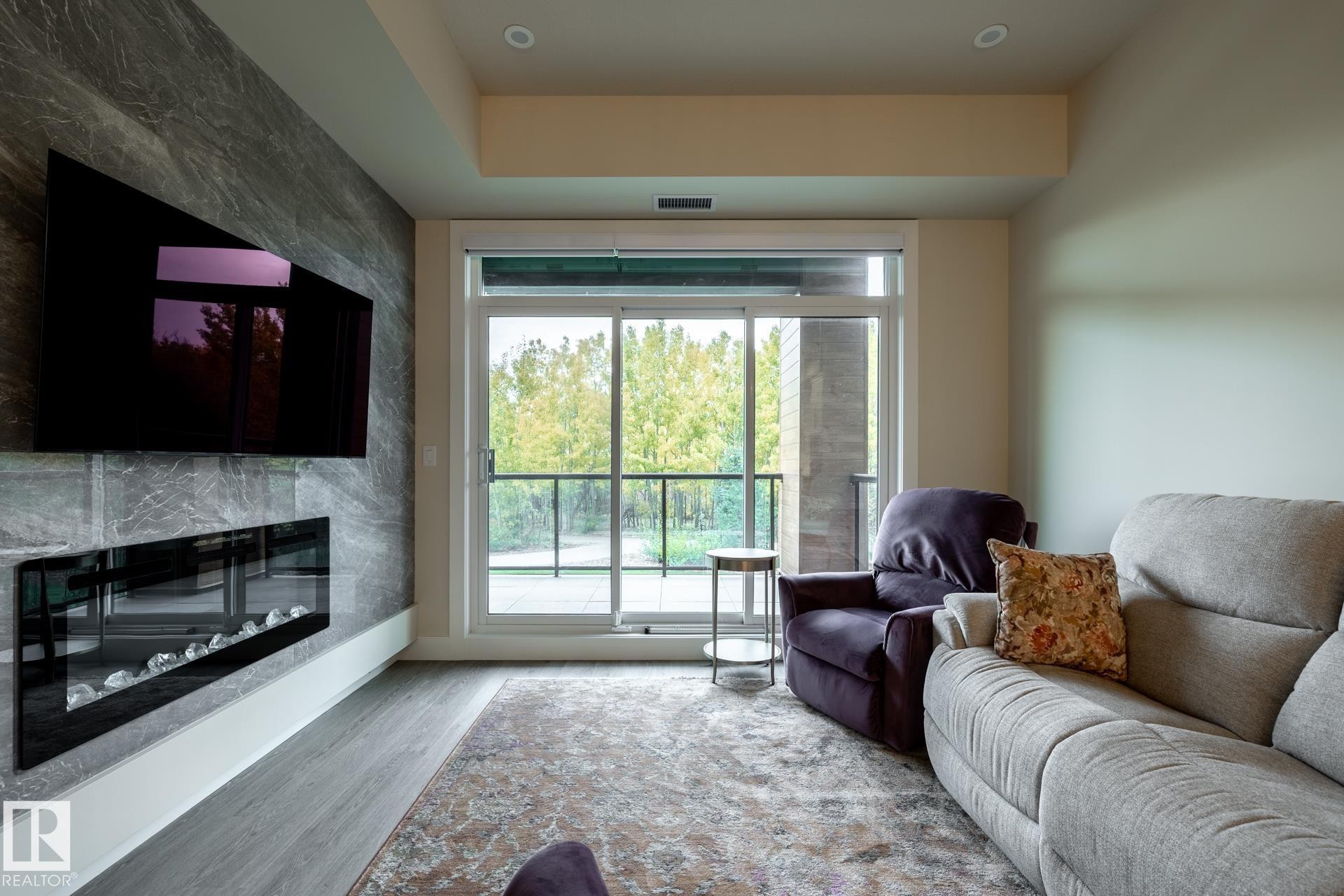 Living area featuring a high end fireplace and wood finished floors - 112 7471 May Common, Edmonton, AB - Indoor Photo Showing Living Room With Fireplace
