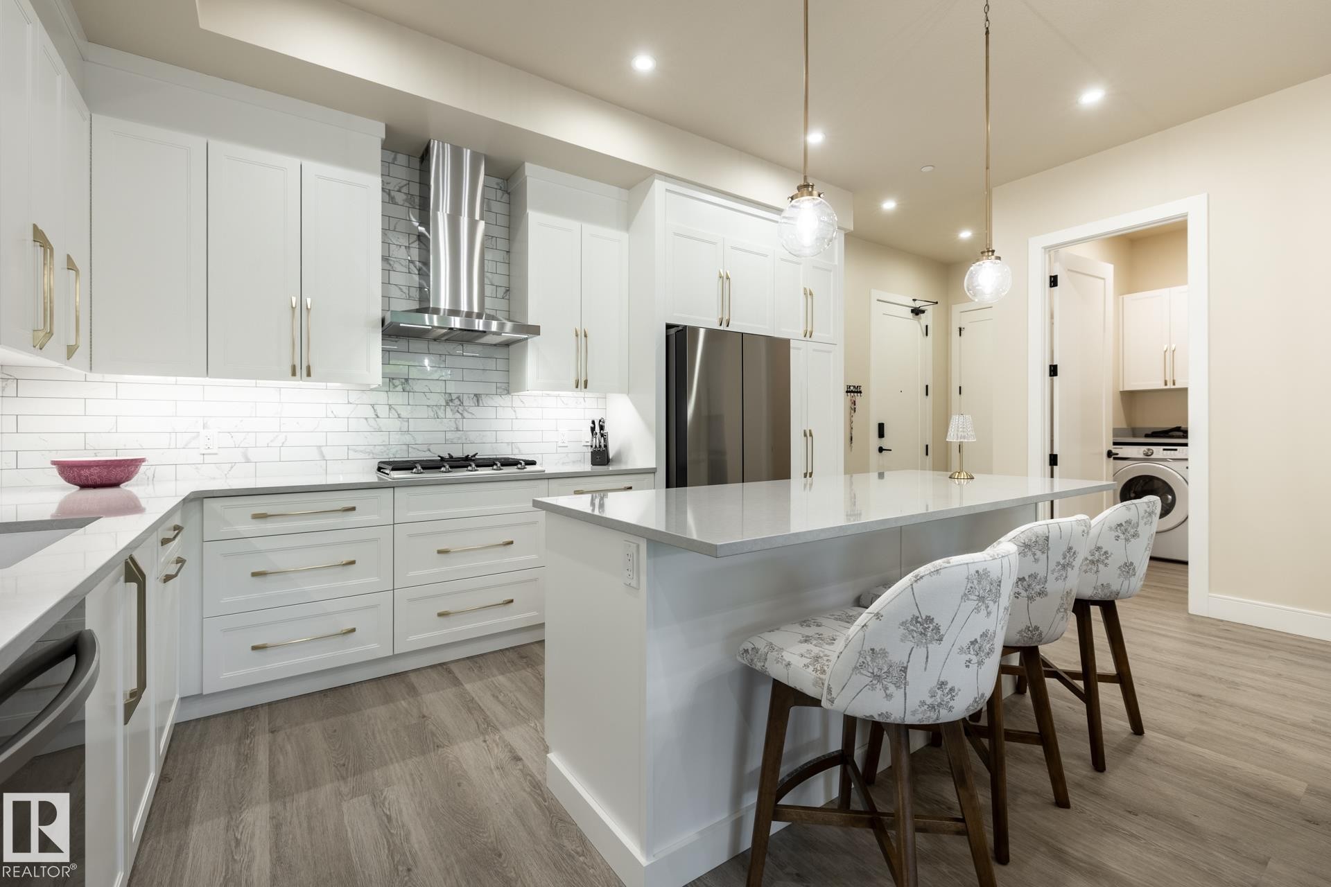 Kitchen featuring a kitchen bar, light wood finished floors, light stone countertops, wall chimney range hood, and white cabinets - 112 7471 May Common, Edmonton, AB - Indoor Photo Showing Kitchen With Upgraded Kitchen