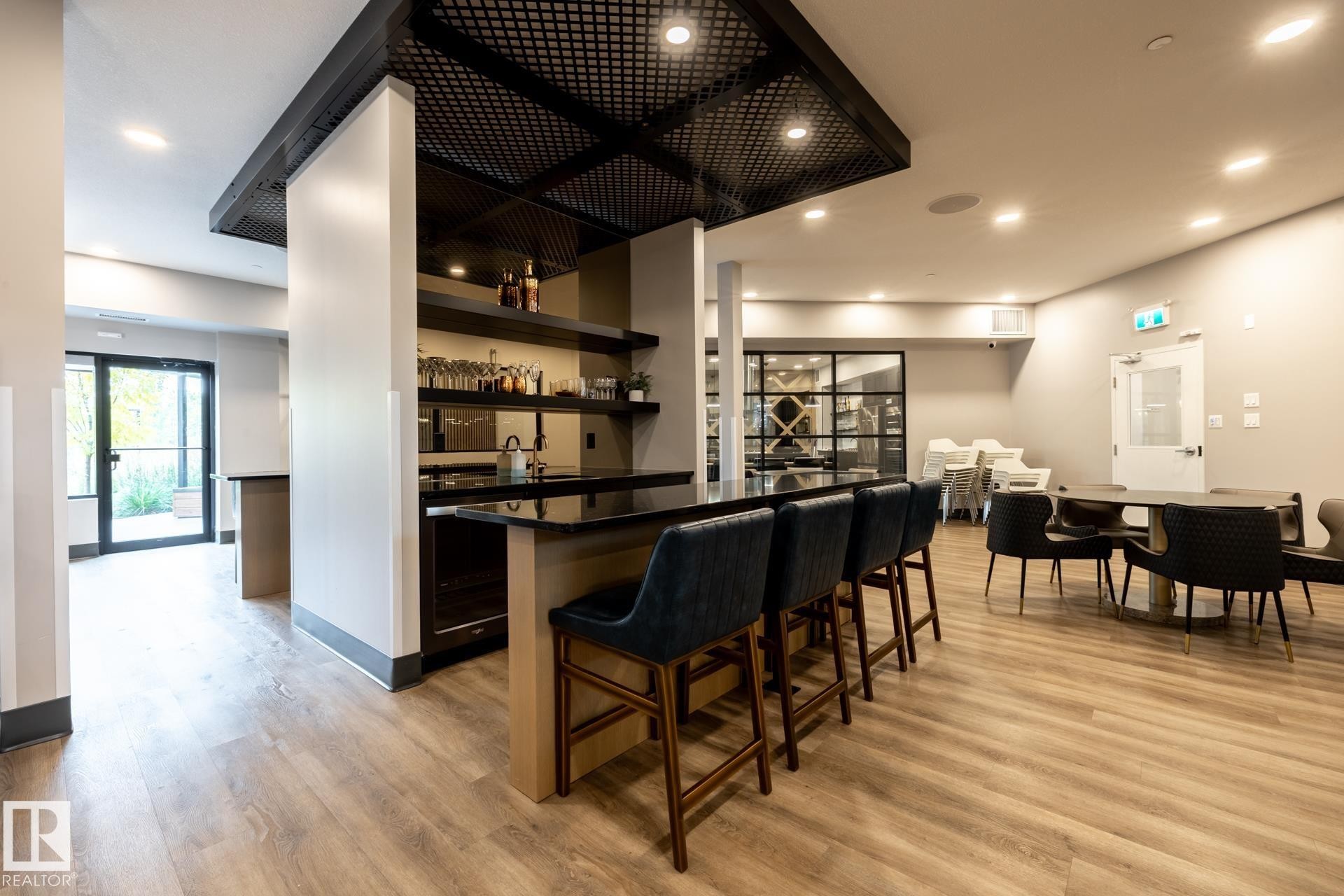 Indoor wet bar featuring open shelves, light wood-style floors, recessed lighting, dark stone countertops, and dark cabinetry - 112 7471 May Common, Edmonton, AB - Indoor Photo Showing Dining Room