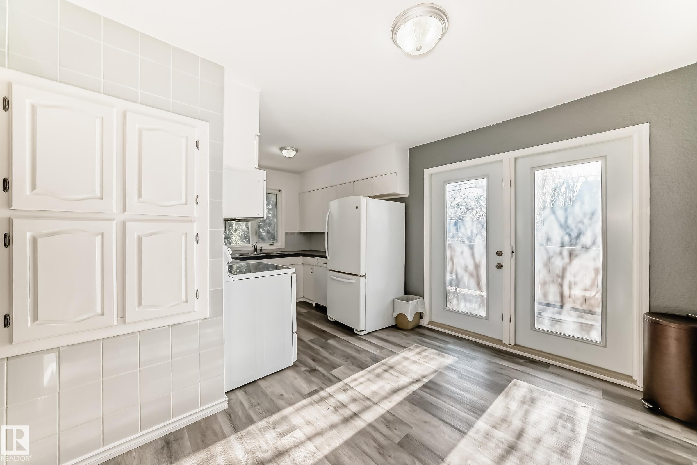 Kitchen with white appliances, white cabinets, dark countertops, and light wood finished floors - 8639 64 Avenue Nw, Edmonton, AB - Indoor Photo Showing Kitchen