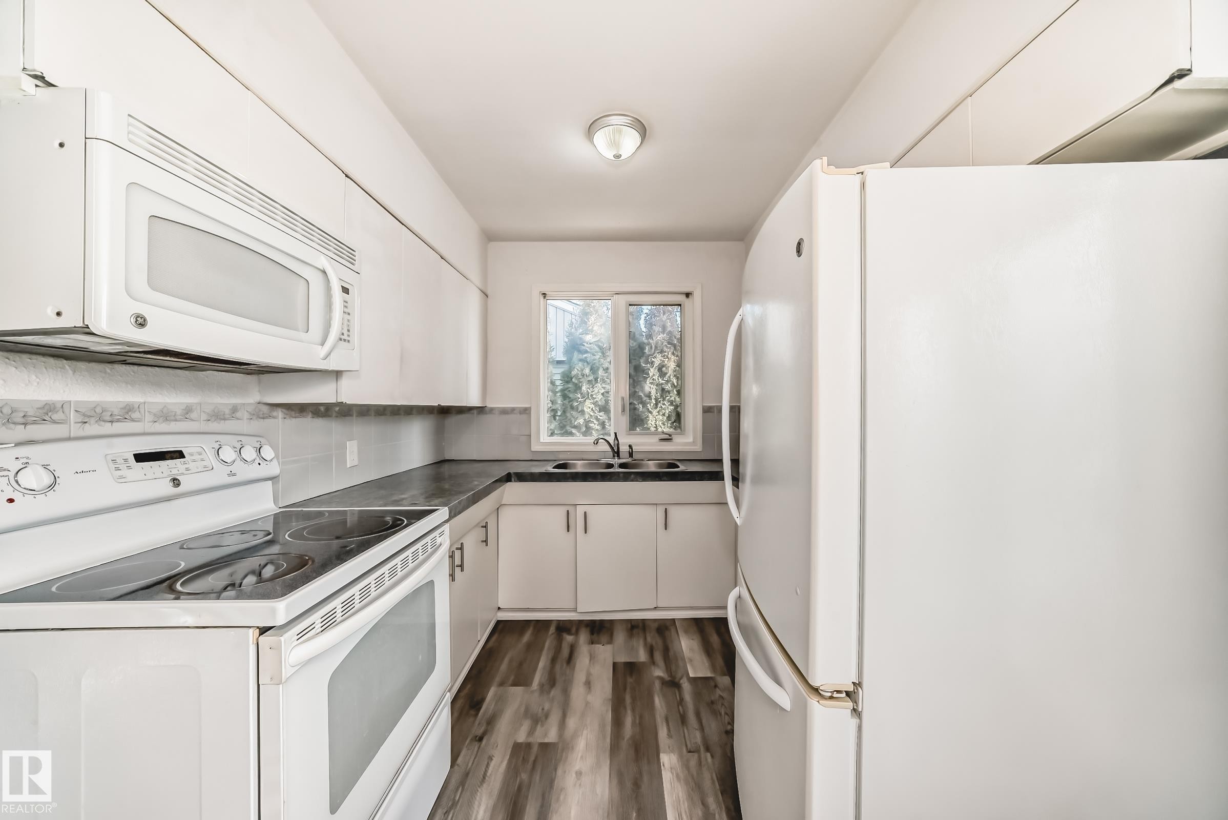 Kitchen with white appliances, white cabinets, dark wood finished floors, and dark countertops - 8639 64 Avenue Nw, Edmonton, AB - Indoor Photo Showing Kitchen With Double Sink