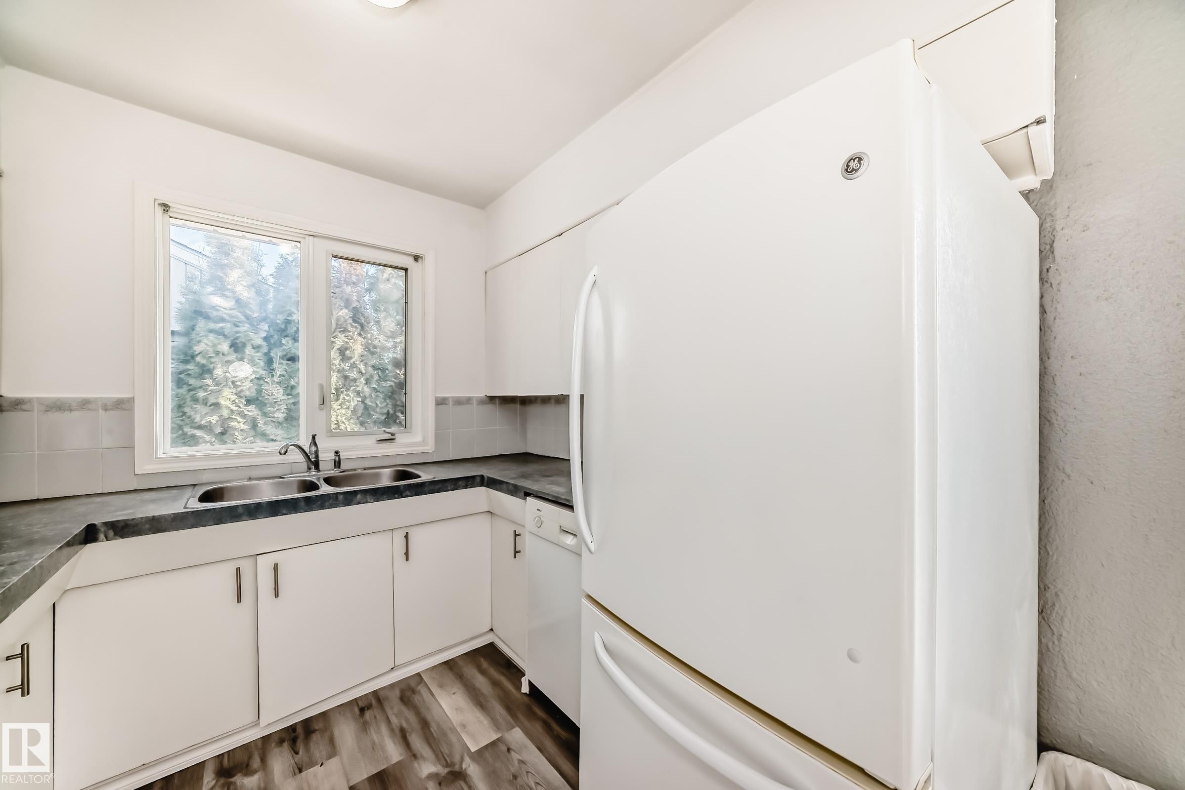 Kitchen featuring white appliances, dark countertops, white cabinets, and dark wood-style floors - 8639 64 Avenue Nw, Edmonton, AB - Indoor Photo Showing Kitchen With Double Sink