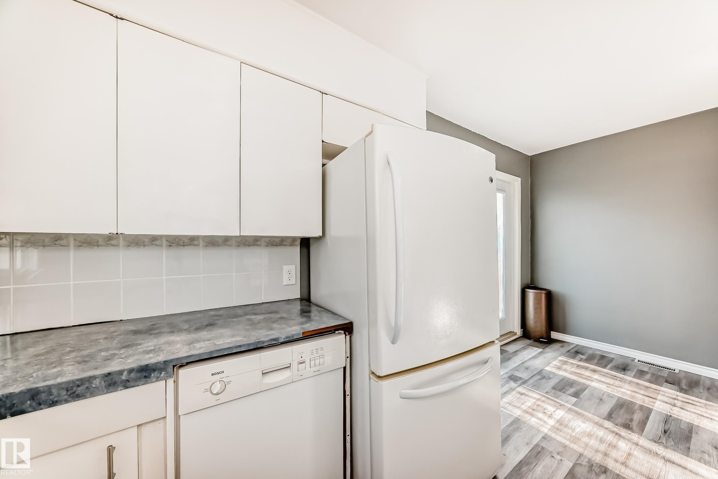 Kitchen featuring white appliances, white cabinets, light wood-style floors, dark countertops, and decorative backsplash - 8639 64 Avenue Nw, Edmonton, AB - Indoor