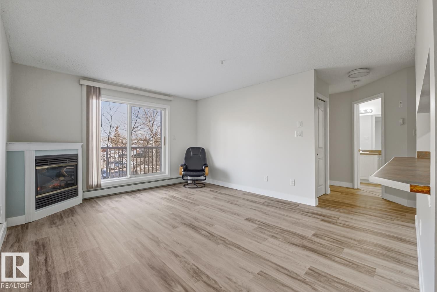 This room features light-toned flooring, a fireplace, and a large window with a view - 237 17447 98A Avenue, Edmonton, AB - Indoor Photo Showing Living Room With Fireplace