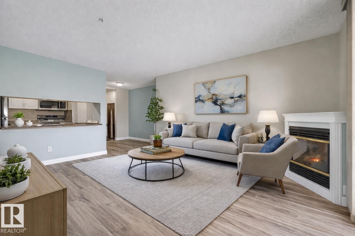 The inviting living room features hardwood flooring, a corner fireplace, and a pass-through window to the kitchen area - 237 17447 98A Avenue, Edmonton, AB - Indoor Photo Showing Living Room With Fireplace