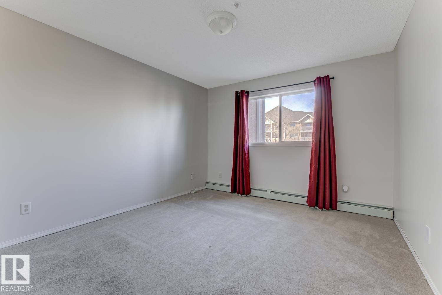 The room features neutral-toned carpet, light gray walls, and a window with a view of nearby structures - 237 17447 98A Avenue, Edmonton, AB - Indoor Photo Showing Other Room