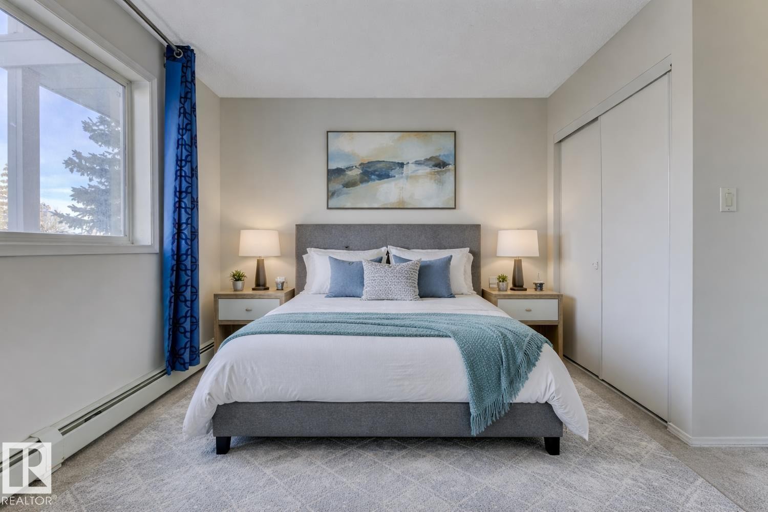 This inviting space features light-colored walls, a large window with blue curtains, and a built-in closet with sliding doors - 237 17447 98A Avenue, Edmonton, AB - Indoor Photo Showing Bedroom
