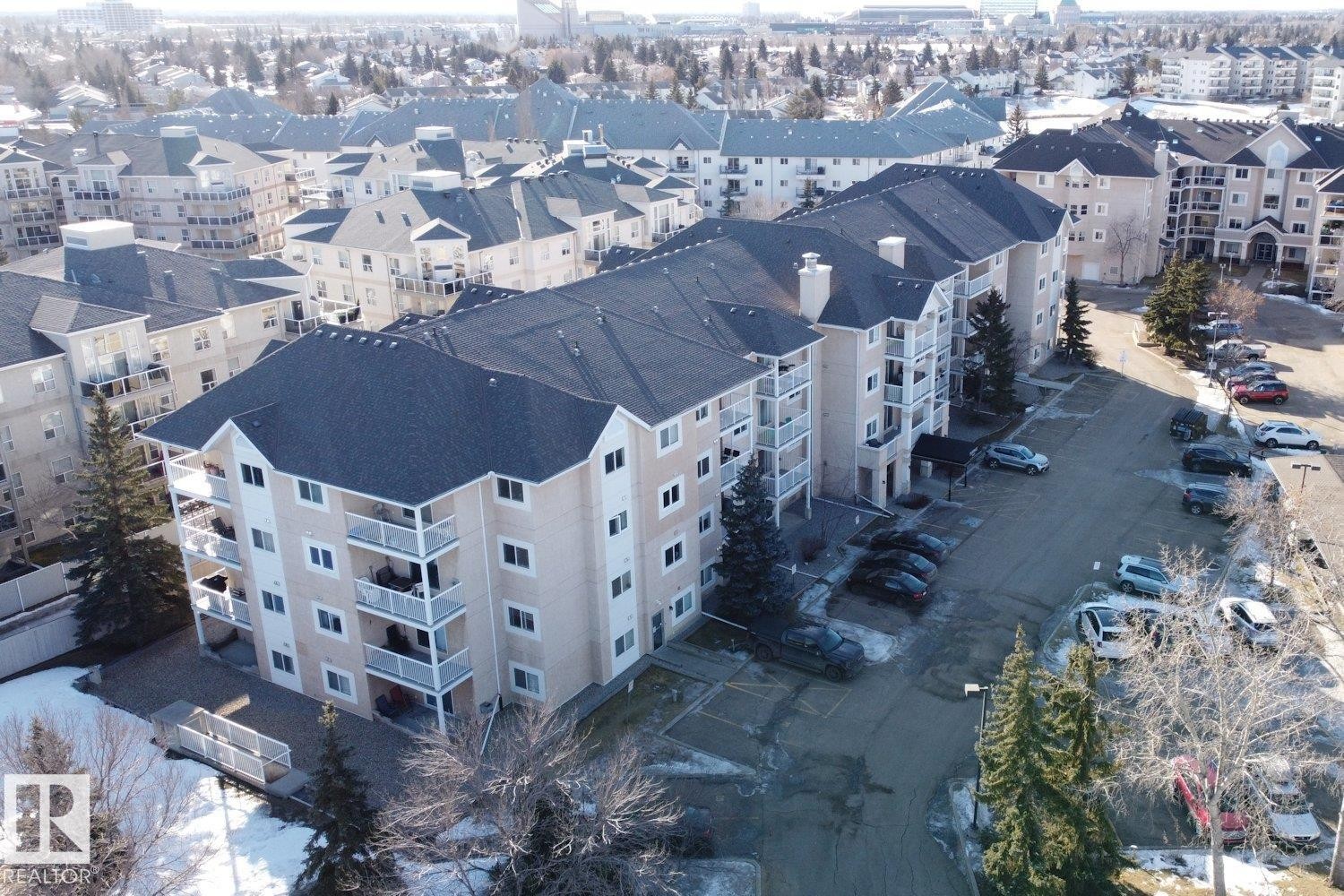 The property features a multi-story building with a dark roof and light-colored siding, offering private balconies and visible parking spaces - 237 17447 98A Avenue, Edmonton, AB - Outdoor With View