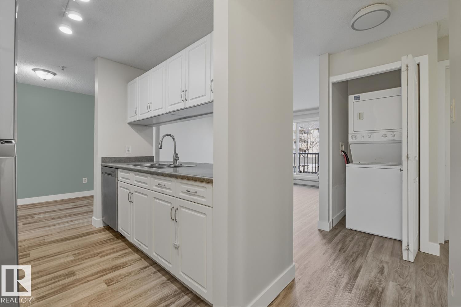 Kitchen with white cabinets, light wood-type flooring, stacked washer / drying machine, and stainless steel appliances - 237 17447 98A Avenue, Edmonton, AB - Indoor