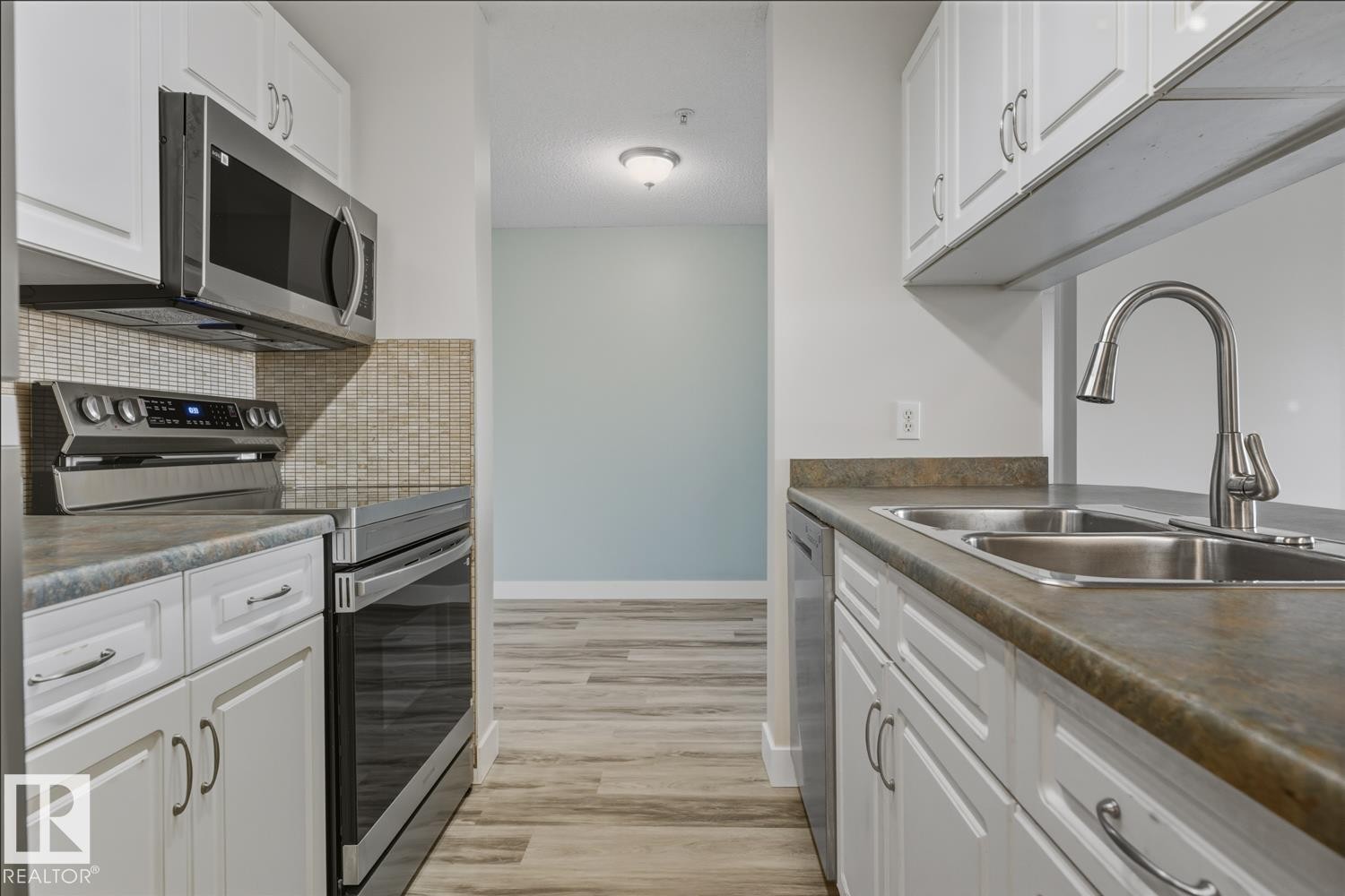 Kitchen with stainless steel appliances, white cabinetry, light wood-type flooring, dark countertops, and tasteful backsplash - 237 17447 98A Avenue, Edmonton, AB - Indoor Photo Showing Kitchen With Double Sink