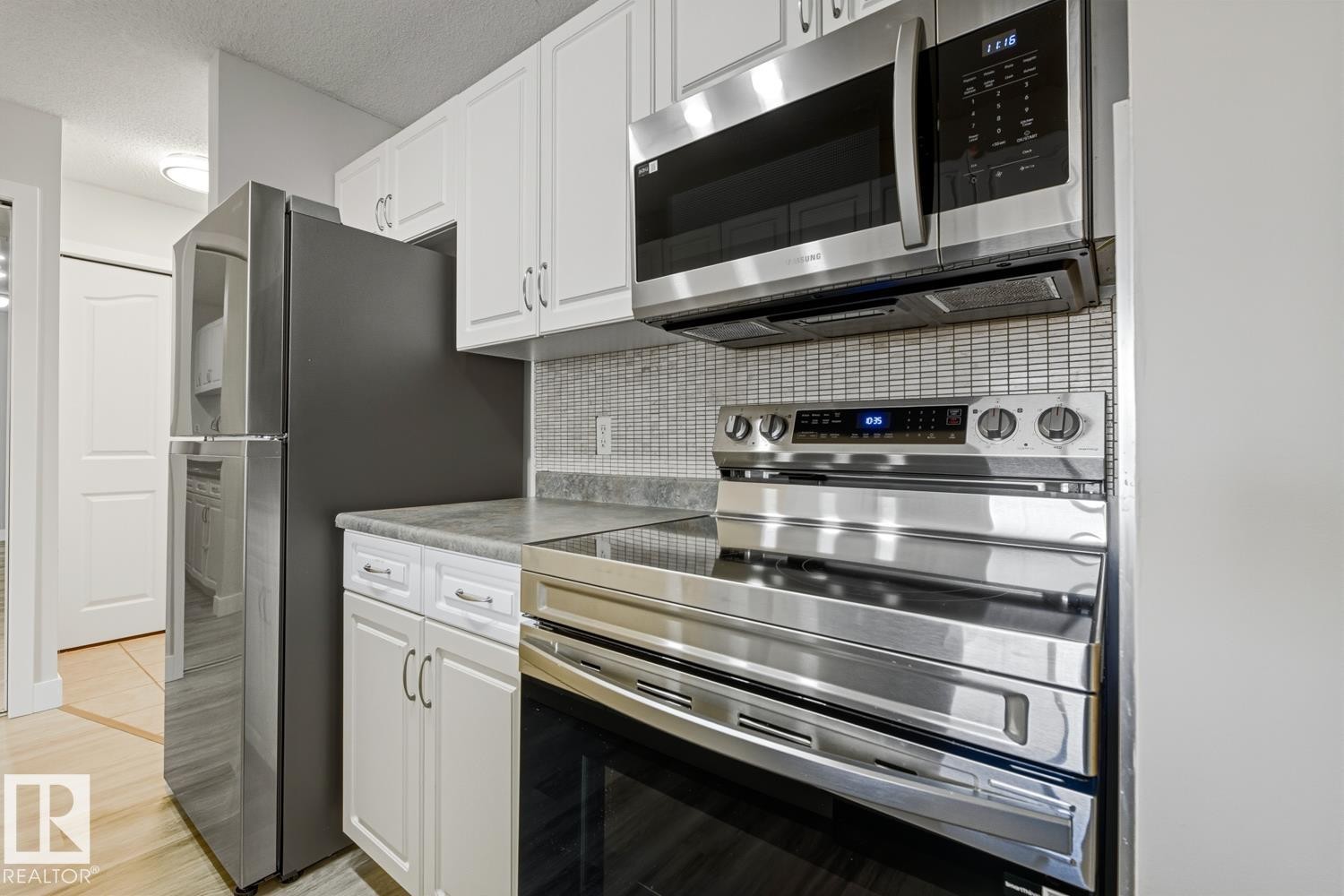 Kitchen with stainless steel appliances, white cabinetry, a textured ceiling, light countertops, and backsplash - 237 17447 98A Avenue, Edmonton, AB - Indoor Photo Showing Kitchen