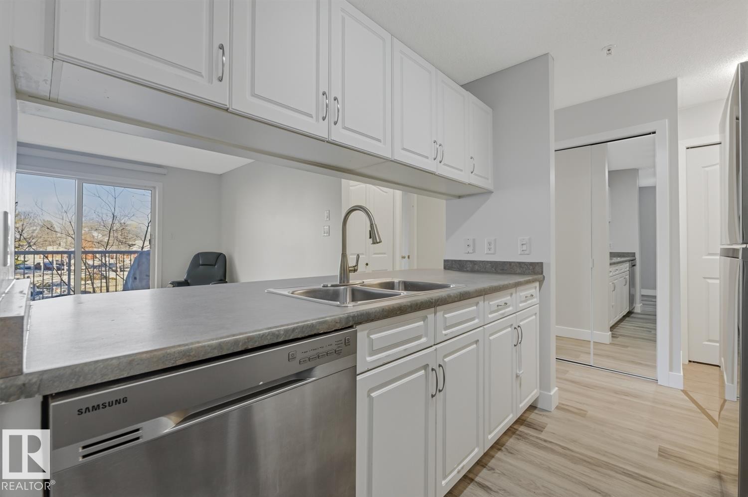 Kitchen with stainless steel dishwasher, white cabinets, light wood-style flooring, dark countertops, and freestanding refrigerator - 237 17447 98A Avenue, Edmonton, AB - Indoor Photo Showing Kitchen With Double Sink