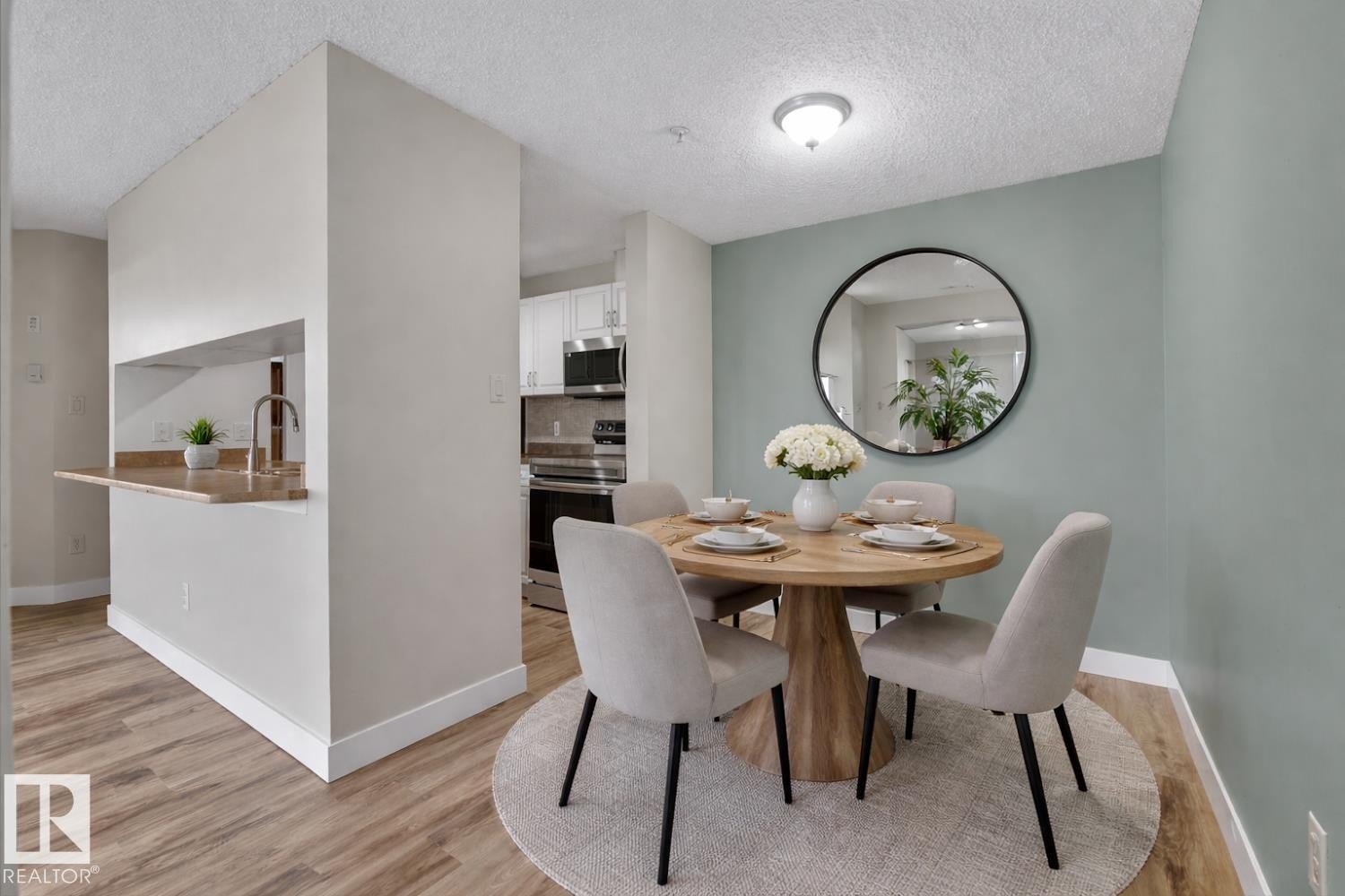 The dining area features a light green accent wall, a circular light wood table, and complementary light-colored seating - 237 17447 98A Avenue, Edmonton, AB - Indoor Photo Showing Dining Room