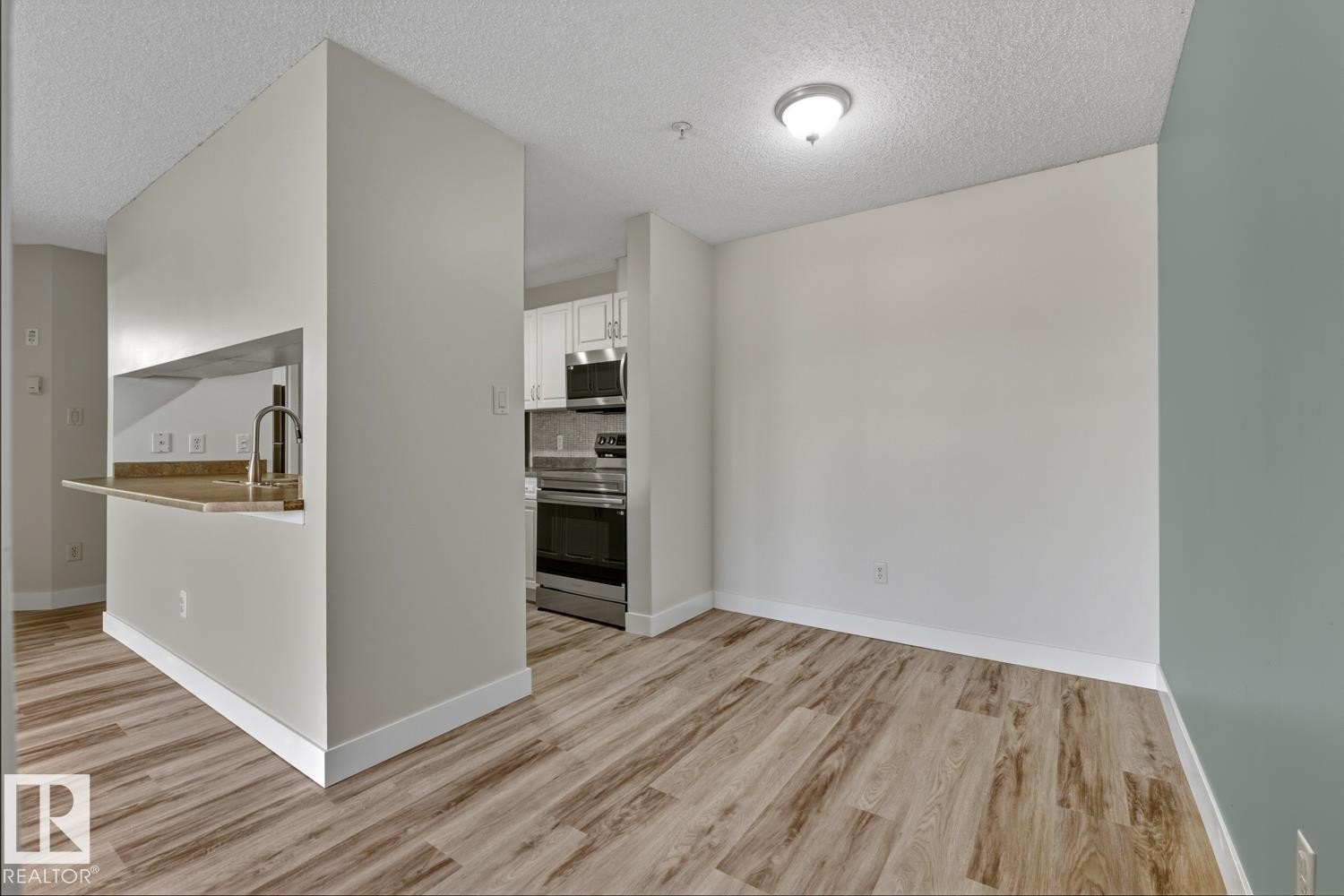 This property features wood-look flooring throughout, a kitchen with white cabinetry and stainless steel appliances, and a breakfast bar with a sink and faucet - 237 17447 98A Avenue, Edmonton, AB - Indoor