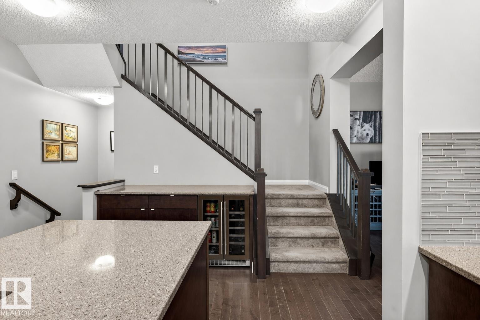 Entryway featuring a carpeted staircase with dark wood railings, hardwood flooring, and a built-in cabinetry unit with an integrated beverage cooler - 17838 60A Street, Edmonton, AB - Indoor