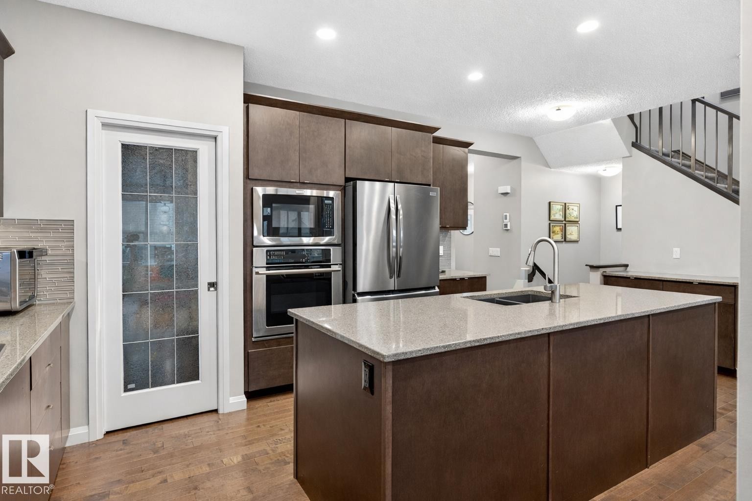 The kitchen features warm-toned cabinetry, stainless steel appliances, and a central island with a sink and light-colored countertop - 17838 60A Street, Edmonton, AB - Indoor Photo Showing Kitchen With Double Sink With Upgraded Kitchen