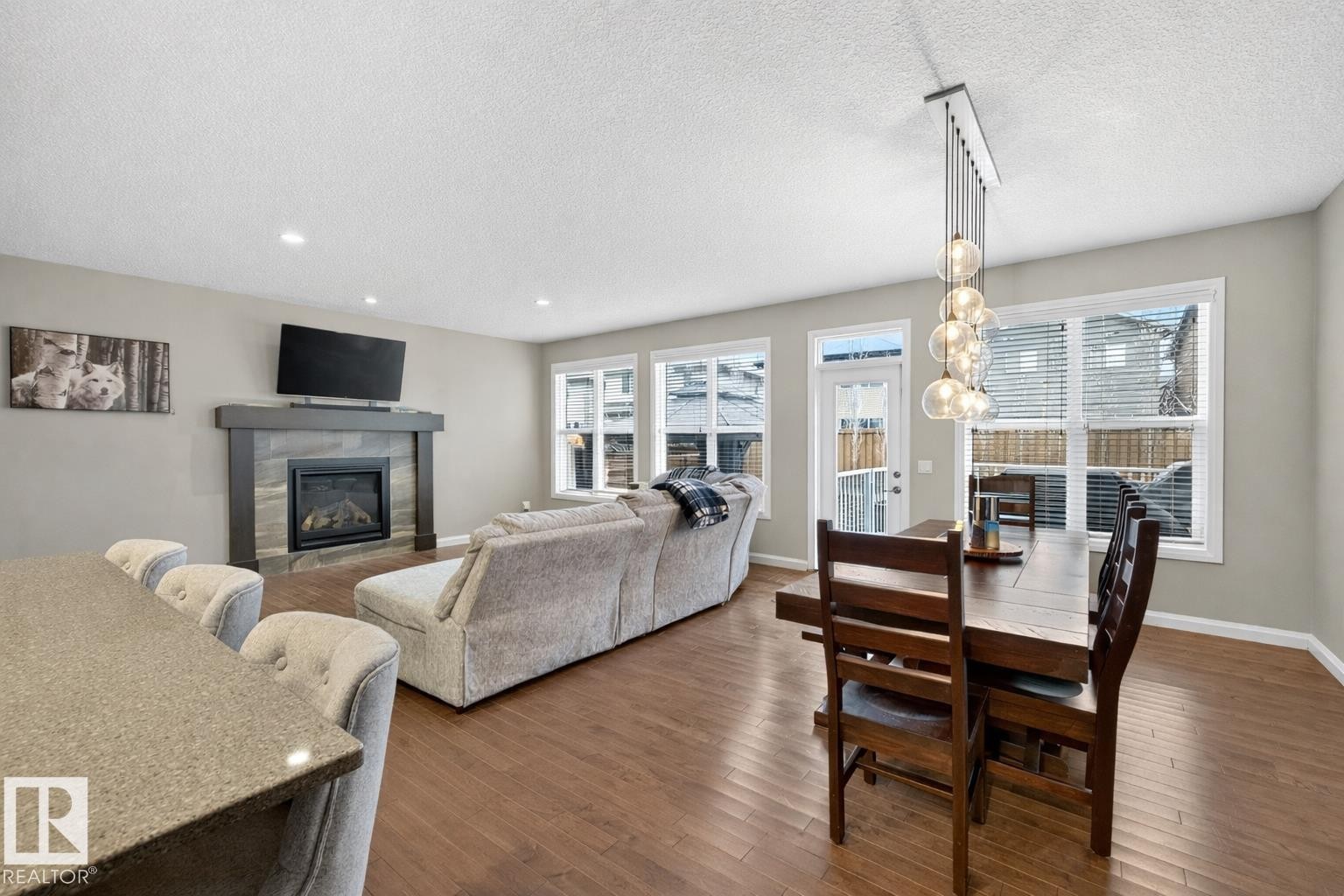 Open concept living area featuring hardwood floors, a gas fireplace with a stone surround, and large windows providing natural light - 17838 60A Street, Edmonton, AB - Indoor With Fireplace
