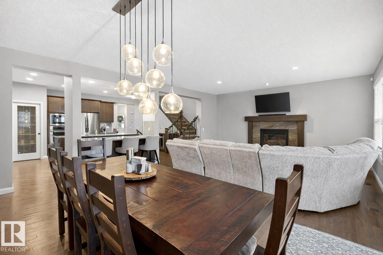 The property features a dining area with a dark wood table and chairs, illuminated by a multi-bulb pendant light fixture - 17838 60A Street, Edmonton, AB - Indoor Photo Showing Dining Room With Fireplace