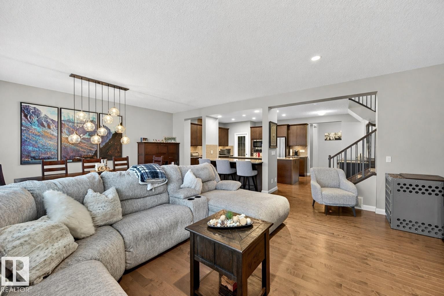 This property features hardwood flooring throughout the main living areas, with a dining area illuminated by a contemporary chandelier - 17838 60A Street, Edmonton, AB - Indoor Photo Showing Living Room