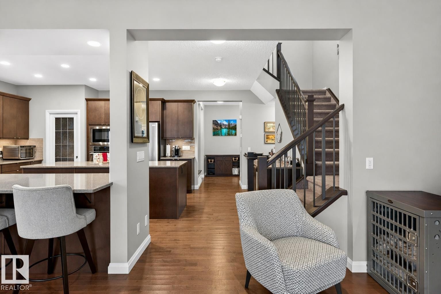 The property features a spacious layout with hardwood flooring, a kitchen with dark wood cabinetry and light-colored countertops, and a staircase with dark wood railings - 17838 60A Street, Edmonton, AB - Indoor